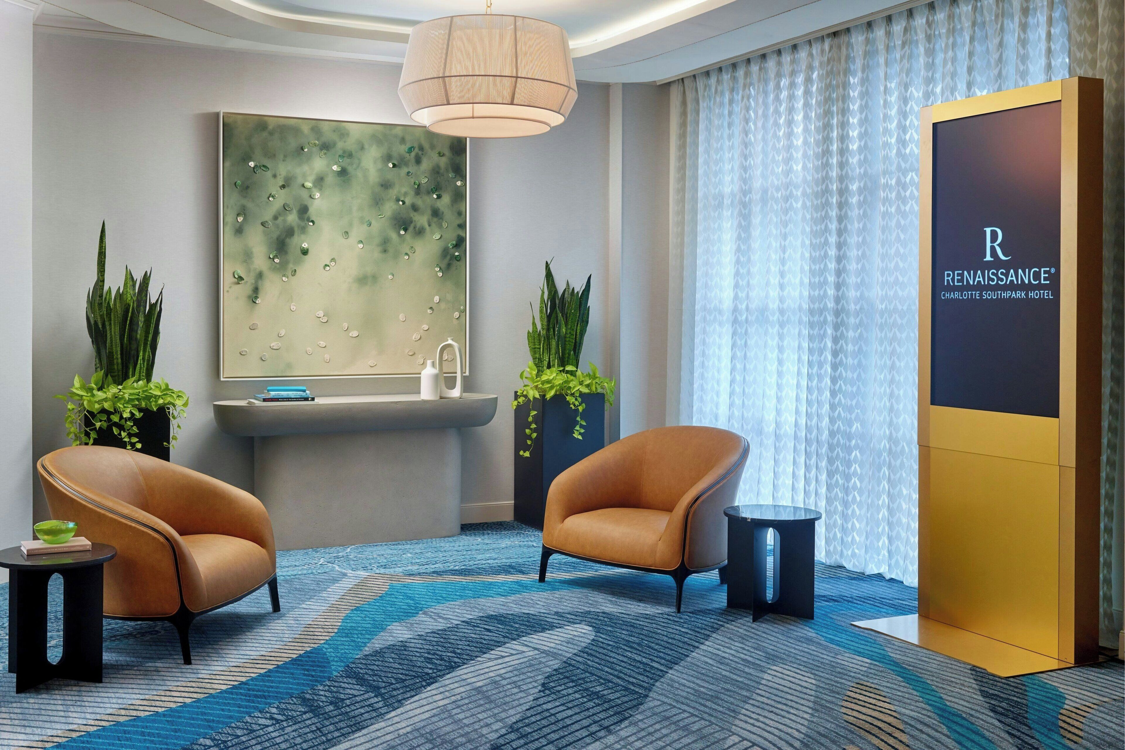 Un vestíbulo moderno con dos sillones de cuero, un cuadro abstracto grande, una mesa de recepción y un amplio ventanal con cortinas.