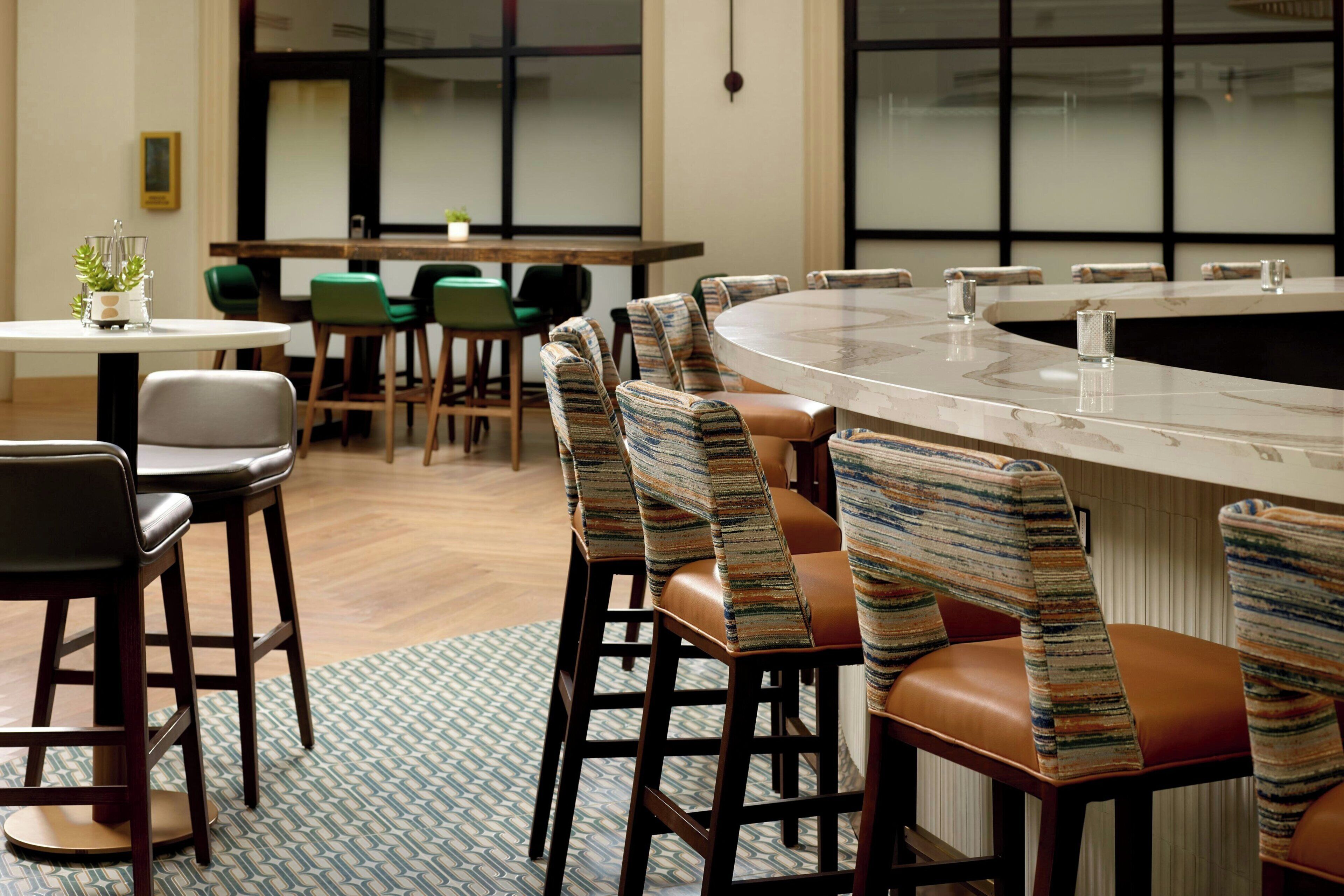 A modern bar area with a marble counter, striped upholstered chairs, and a patterned rug.