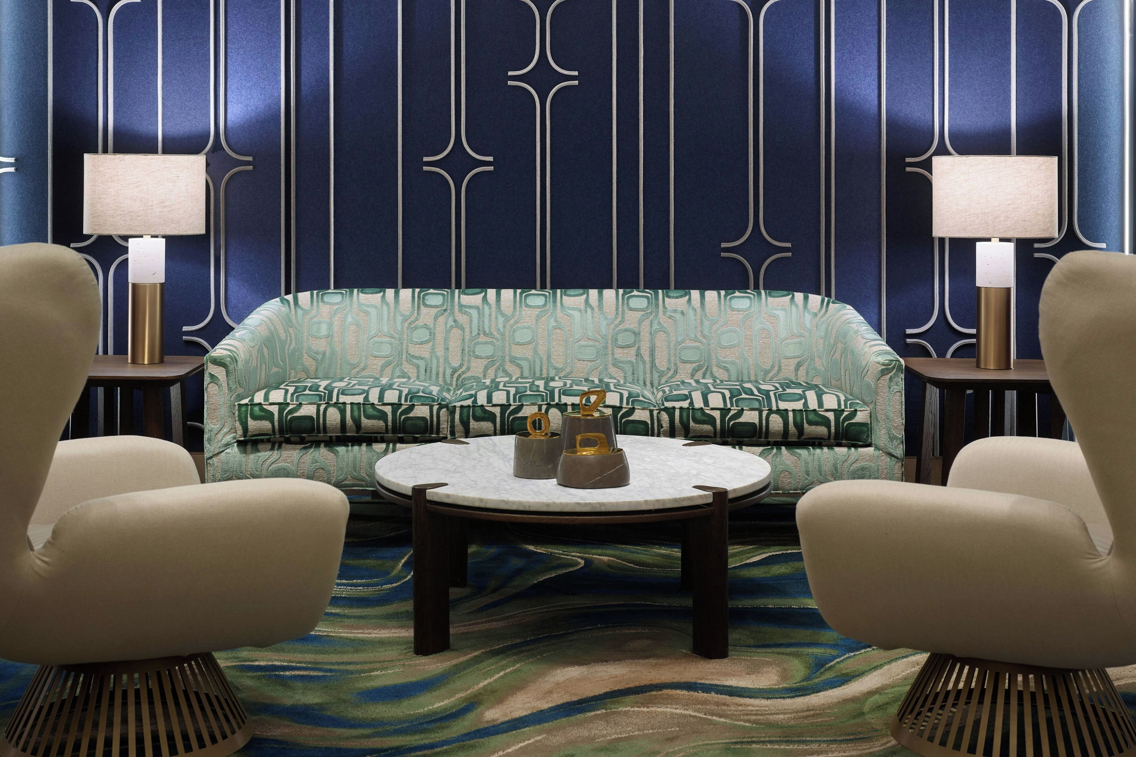 Una habitación con un sofá estampado, dos sillones, una mesa redonda y dos lámparas fijadas a la pared.