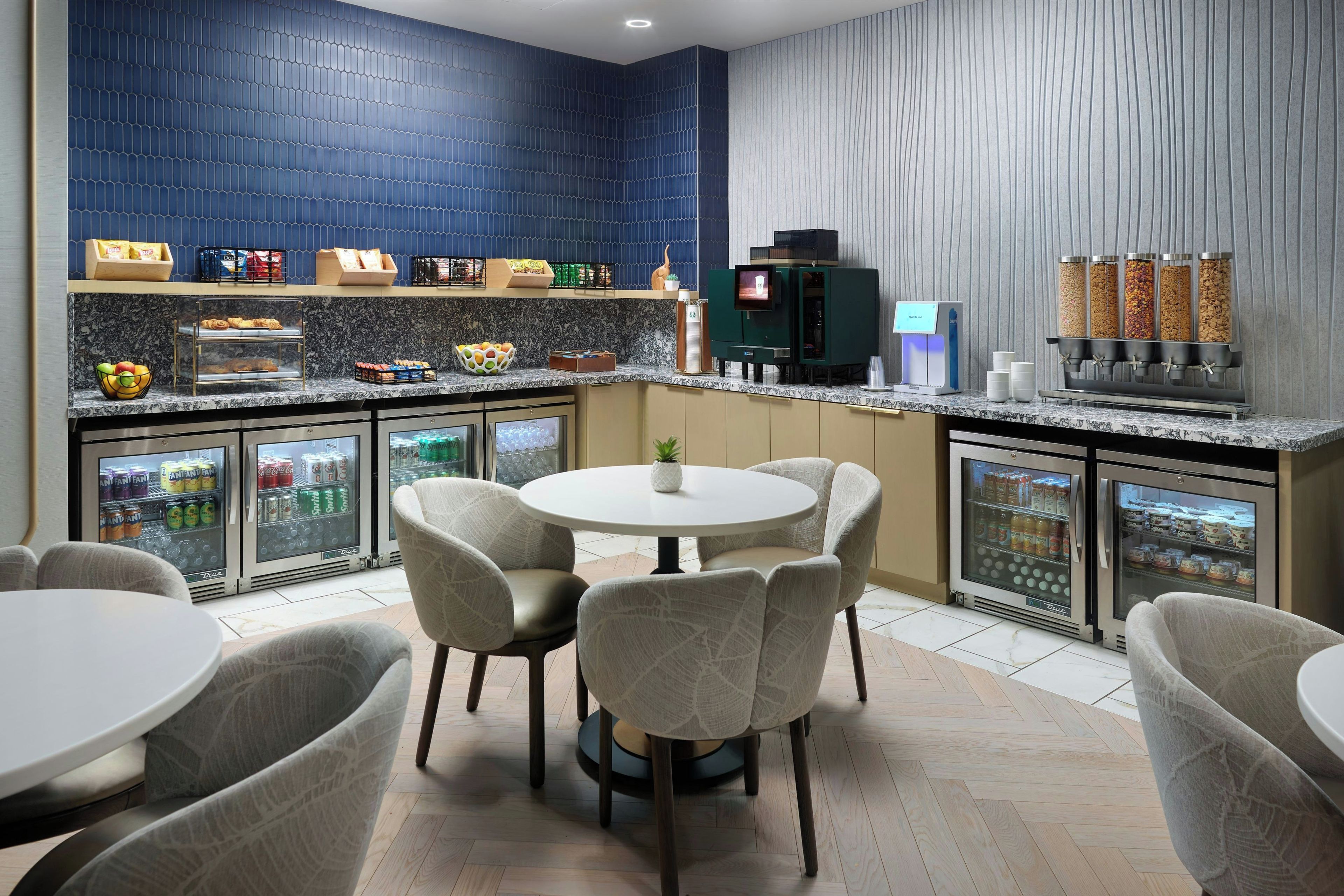 Een moderne keuken met een blauwe achterwand, een koffieapparaat en een koelkast vol drankjes.