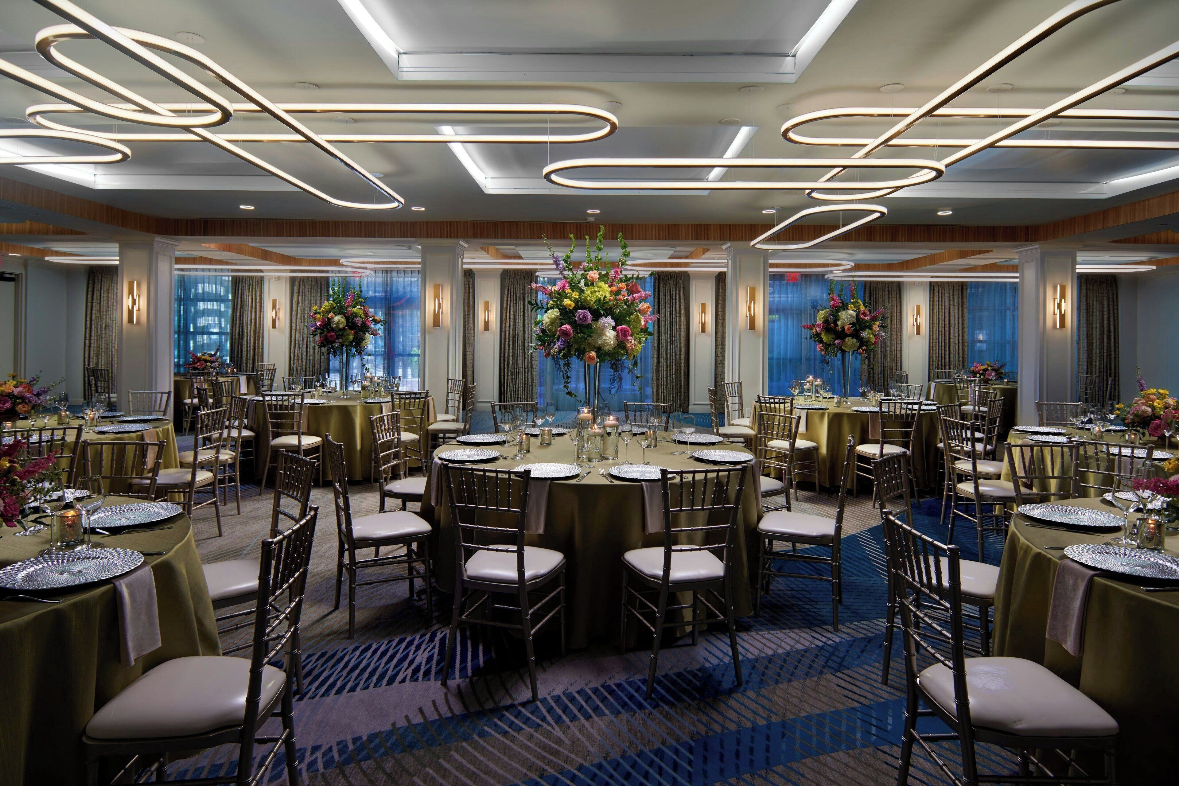 Een feestzaal met ronde tafels, stoelen en bloemdecoraties.