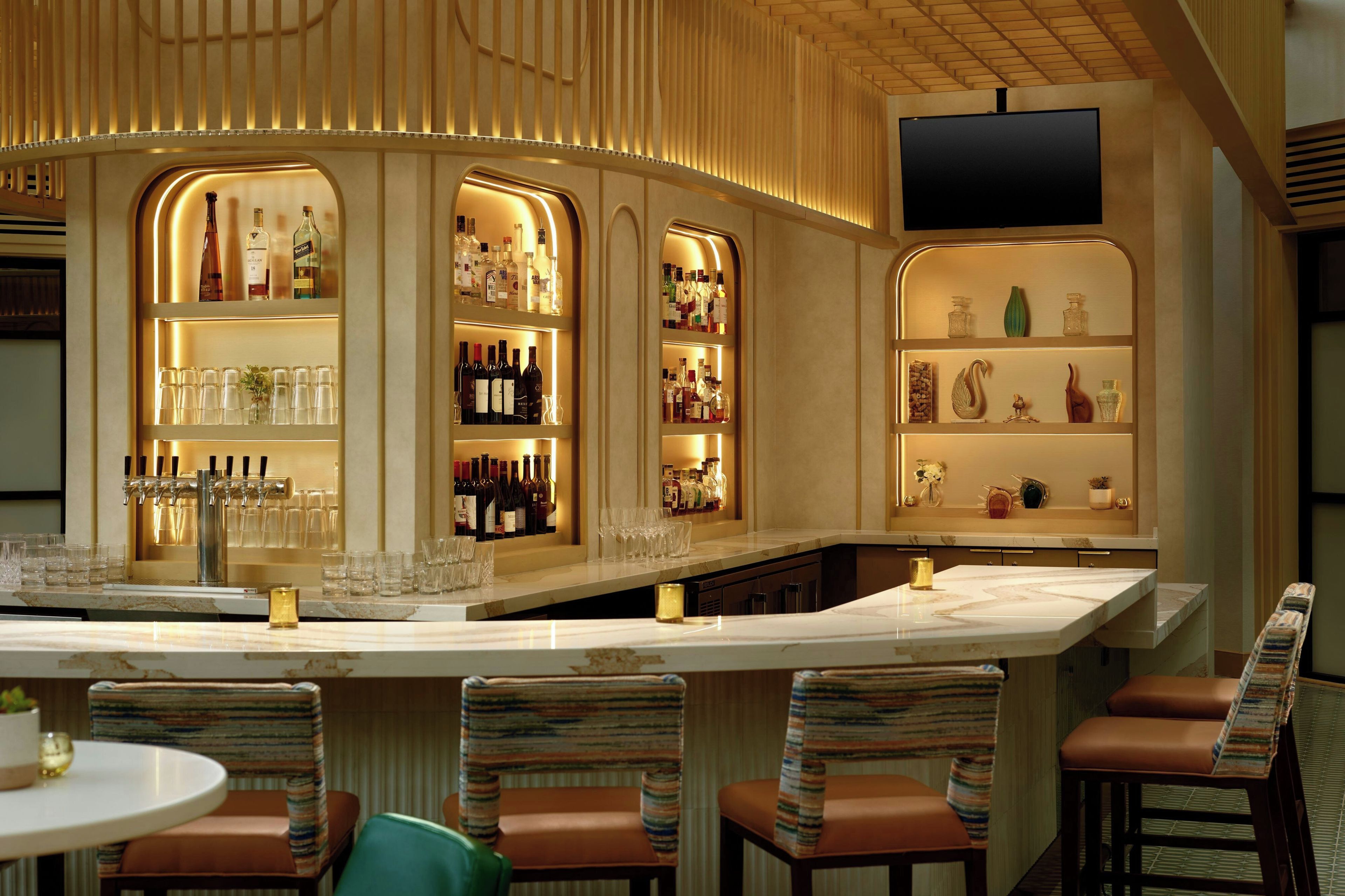 A bar area with a marble countertop, multiple shelves with bottles, and bar stools.