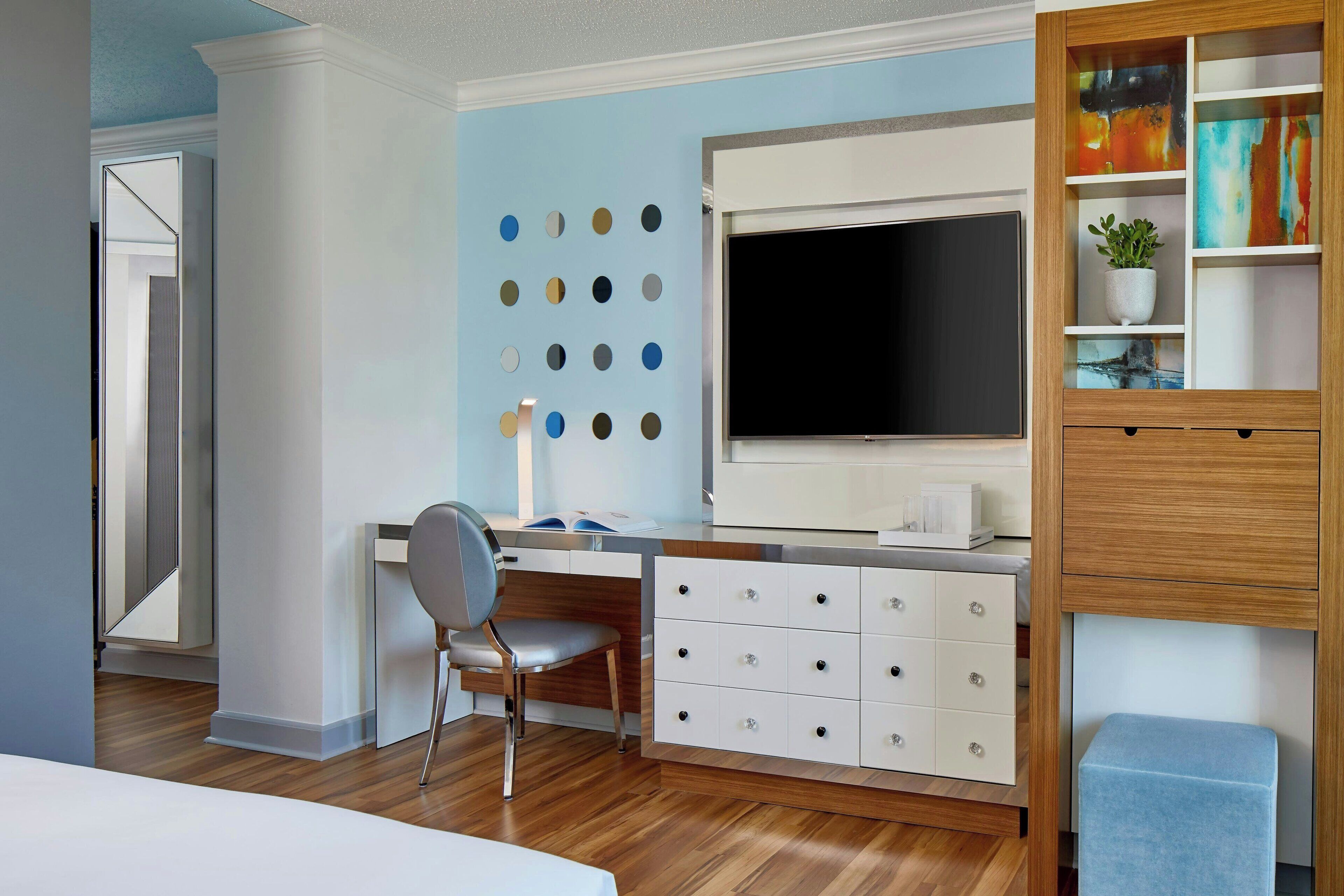 A modern bedroom with a wooden desk, a large TV, and a bookshelf.