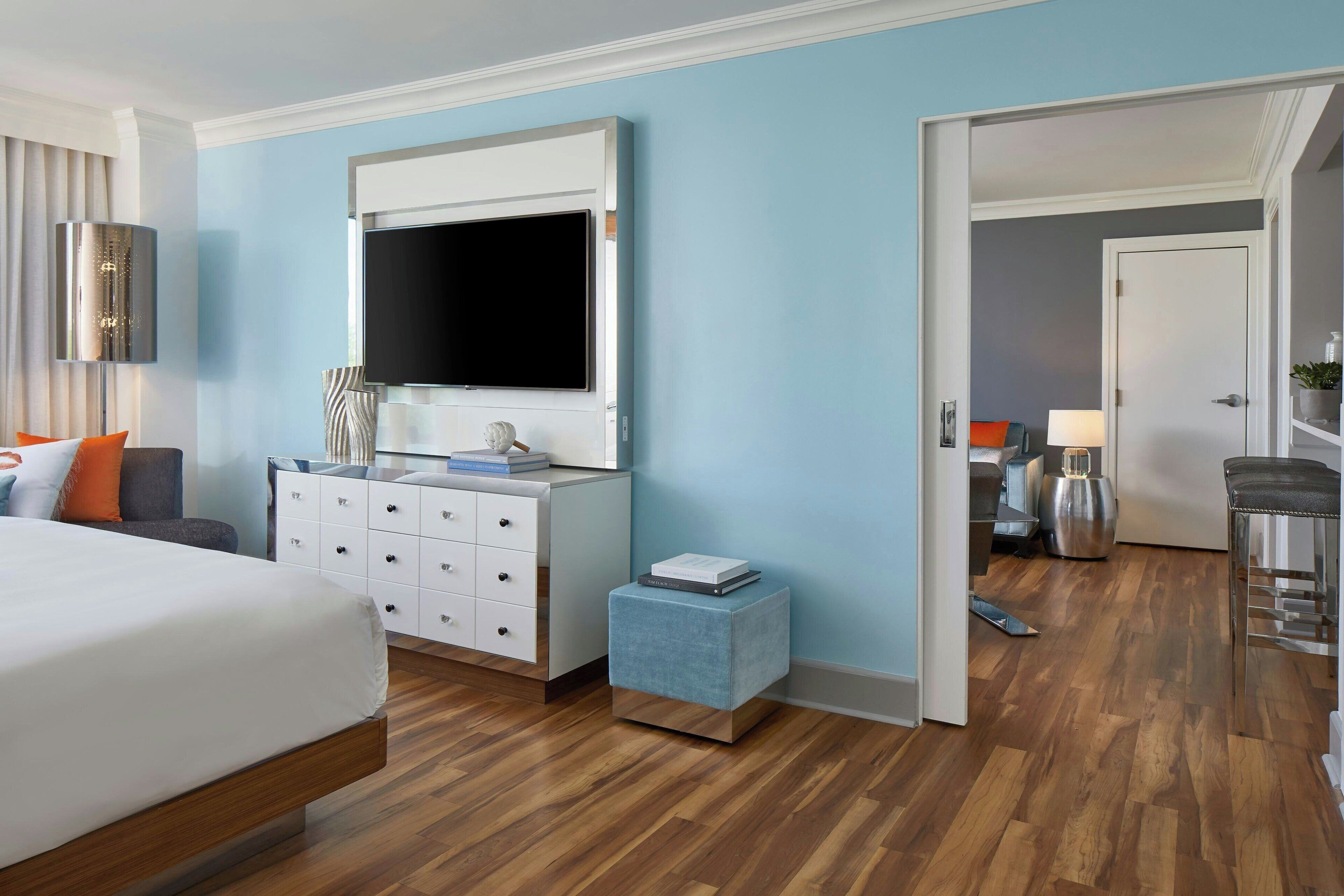 A modern hotel room with a large bed, a dresser with drawers, a small side table, and a television mounted on the wall.