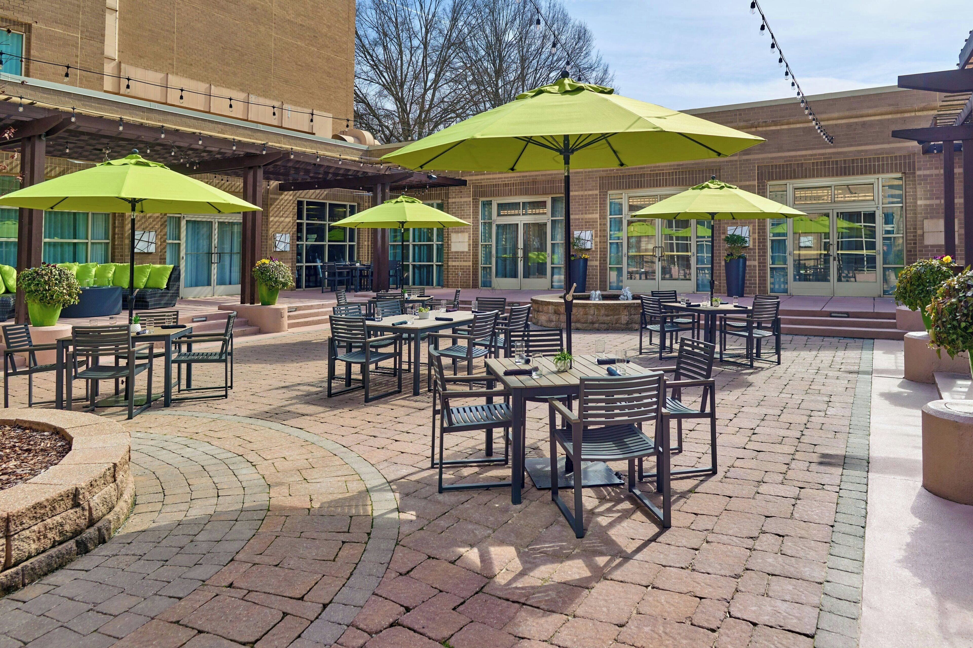 Une terrasse extérieure avec des tables et des chaises, des parasols verts et des plantes en pot.