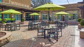 Une terrasse extérieure avec des tables et des chaises, des parasols verts et des plantes en pot.