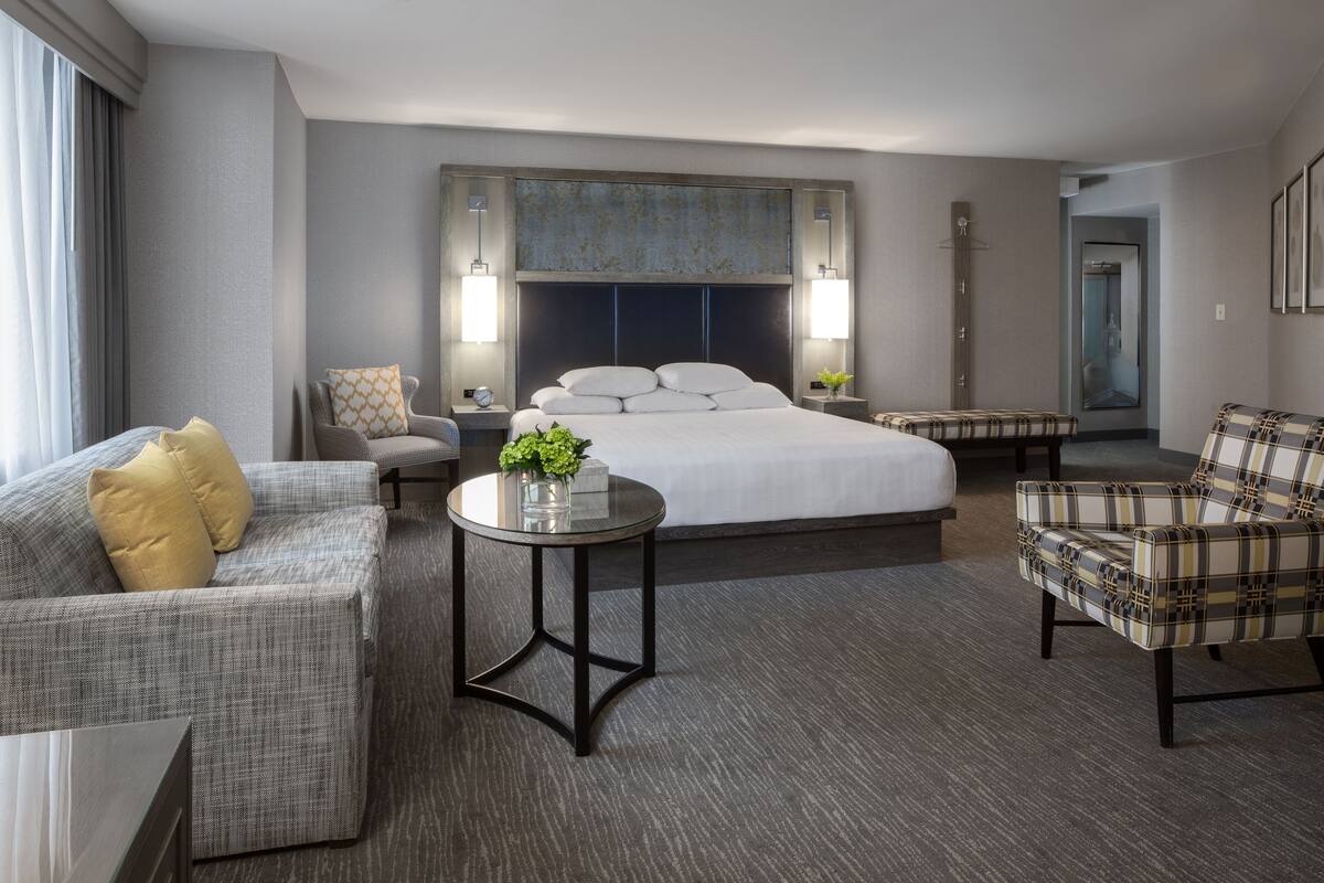 A hotel room with a large bed, two armchairs, a sofa, a small round table, and a mirror.