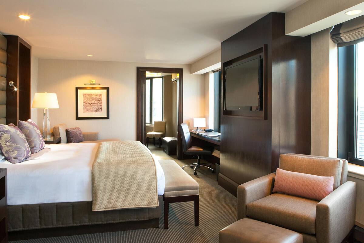 A hotel room with a large bed, a desk, a chair, and a TV.