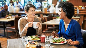 Dos personas cenando en un restaurante con varios platos y bebidas sobre la mesa.