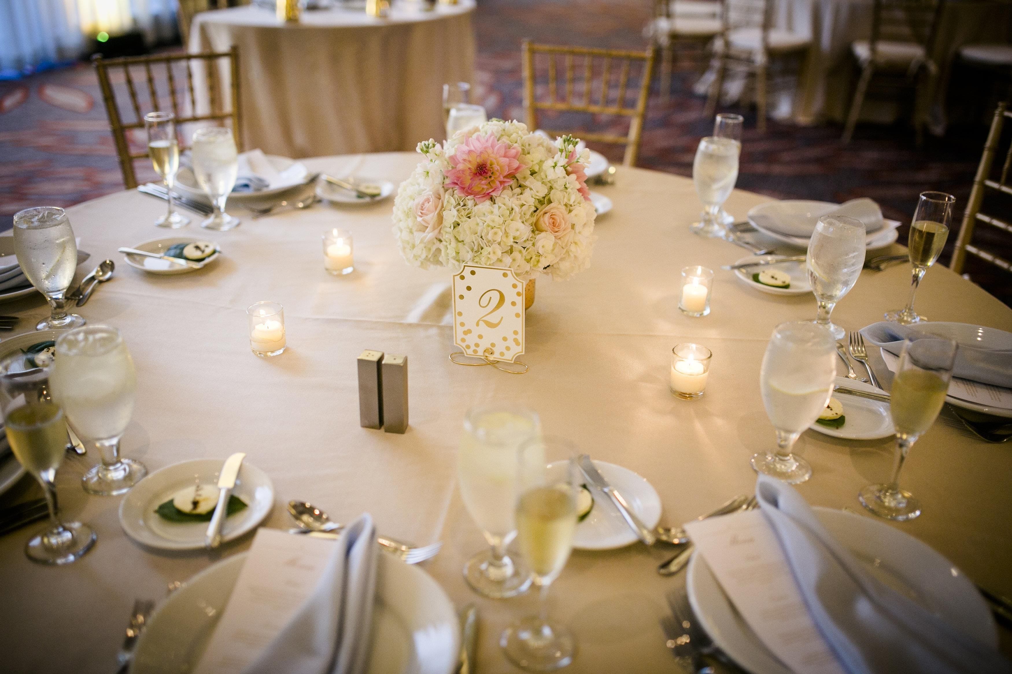 A round table set for a formal event with a floral centerpiece, candles, and glassware.