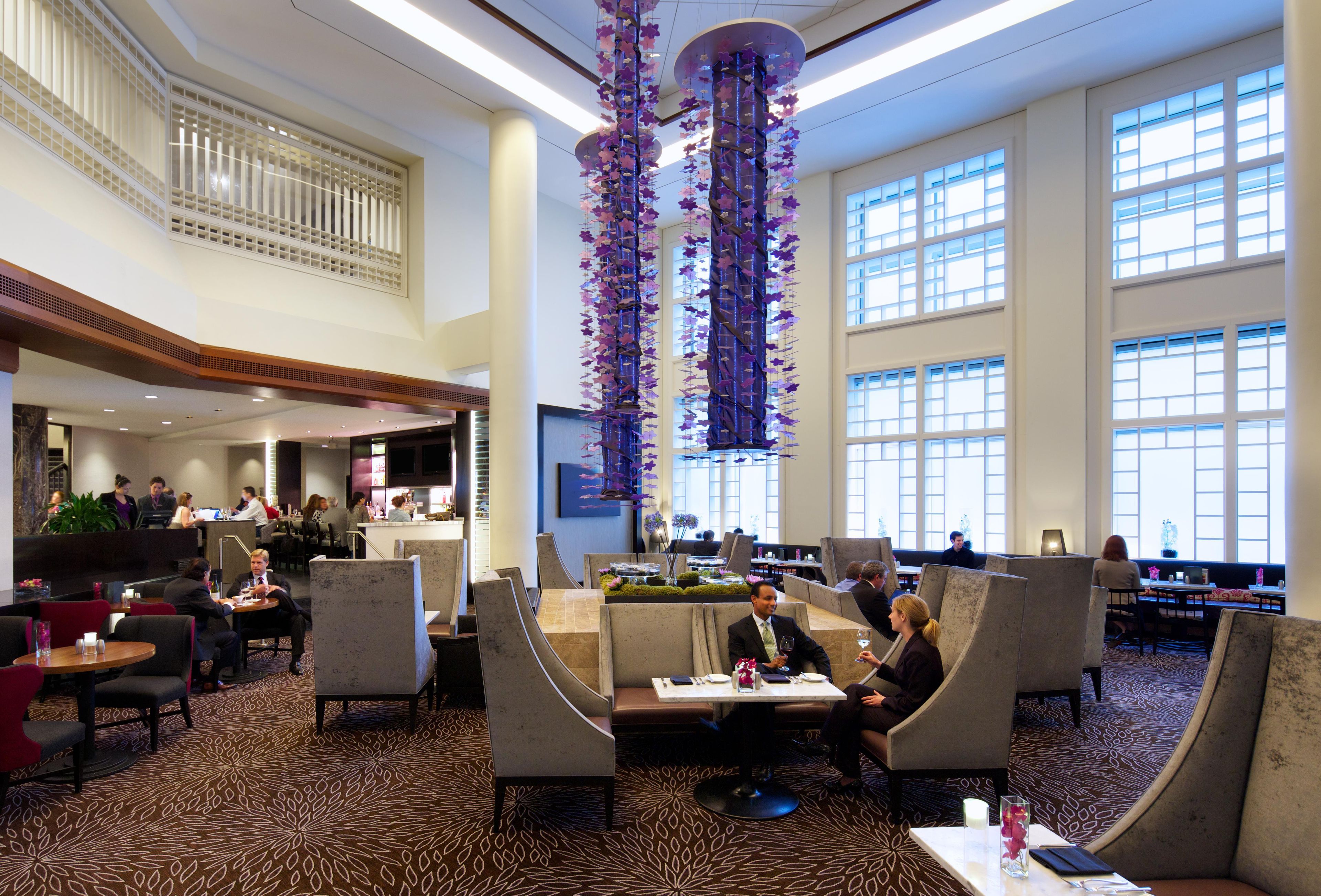 A hotel lobby with high ceilings, a central decorative column, and a seating area with tables and chairs.