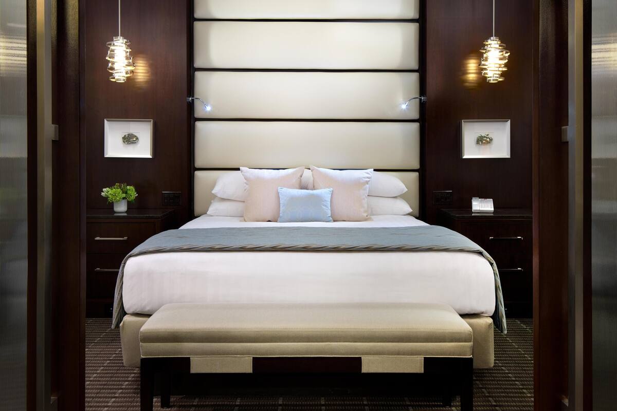 A modern hotel room with a large bed, bedside tables, and wall-mounted lighting.