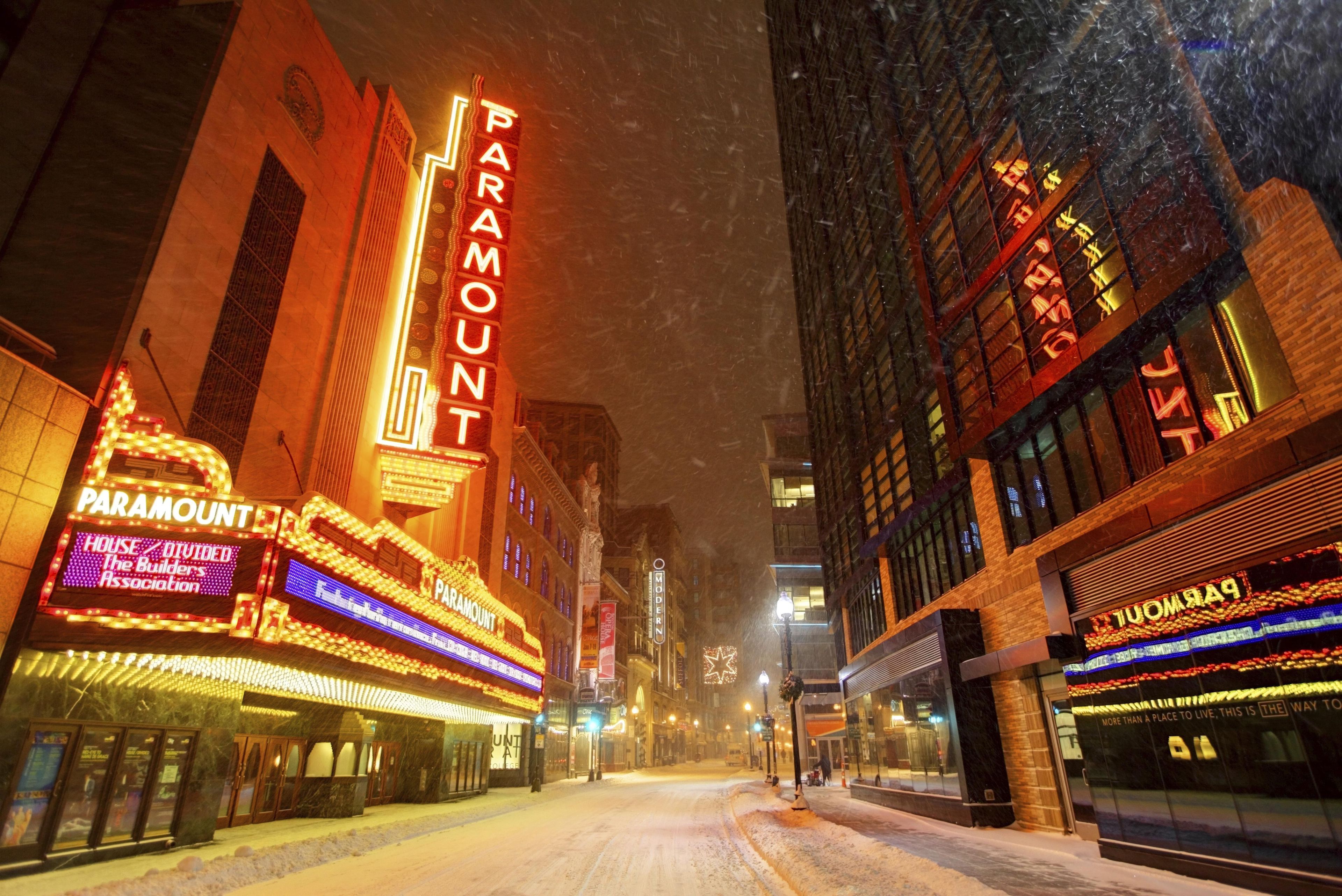 Een met sneeuw bedekte straat met verlichte gebouwen, waaronder een opvallende Paramount theater.