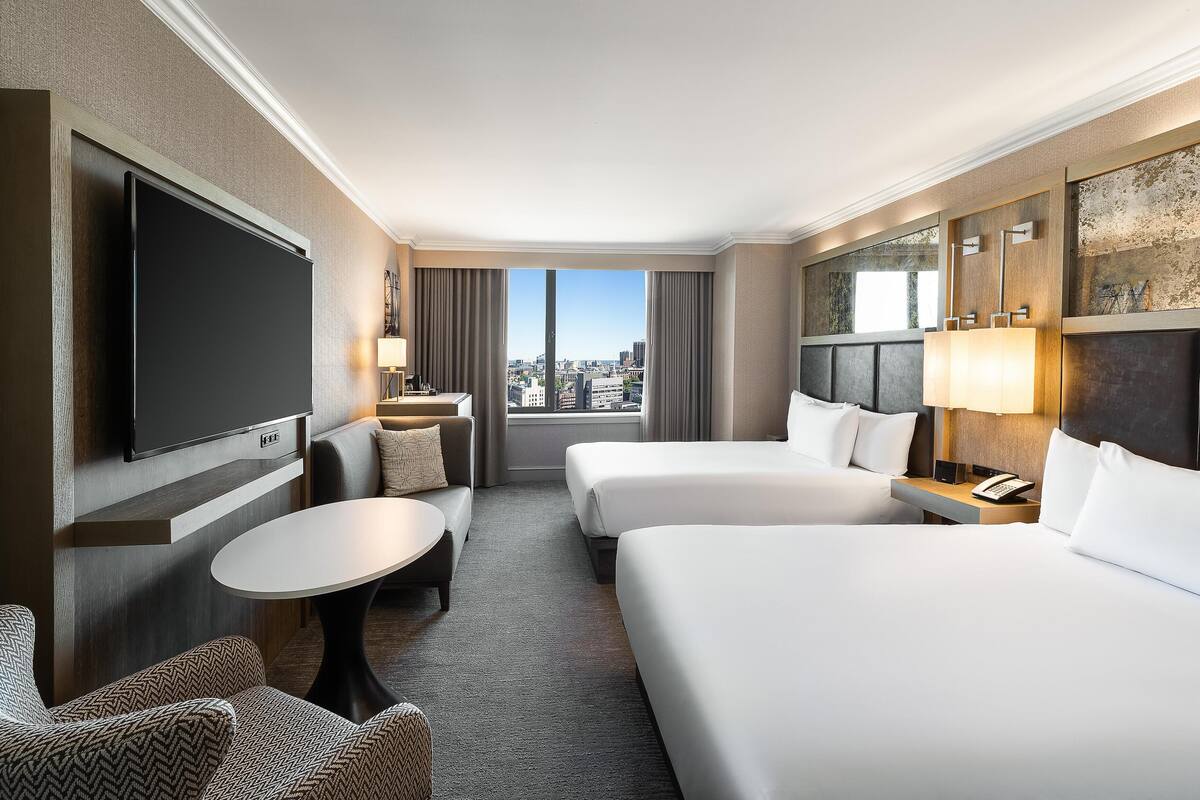 A hotel room with two beds, a TV, a sofa, a small table, and a city view.