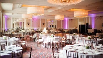 A banquet hall with round tables, chairs, and chandeliers.