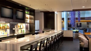 Un bar moderno con una barra alargada, diversas opciones de asientos y vistas panorámicas de la ciudad a través de amplios ventanales.