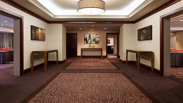 Un pasillo de hotel con alfombra estampada, mesas de madera y obras de arte en las paredes.