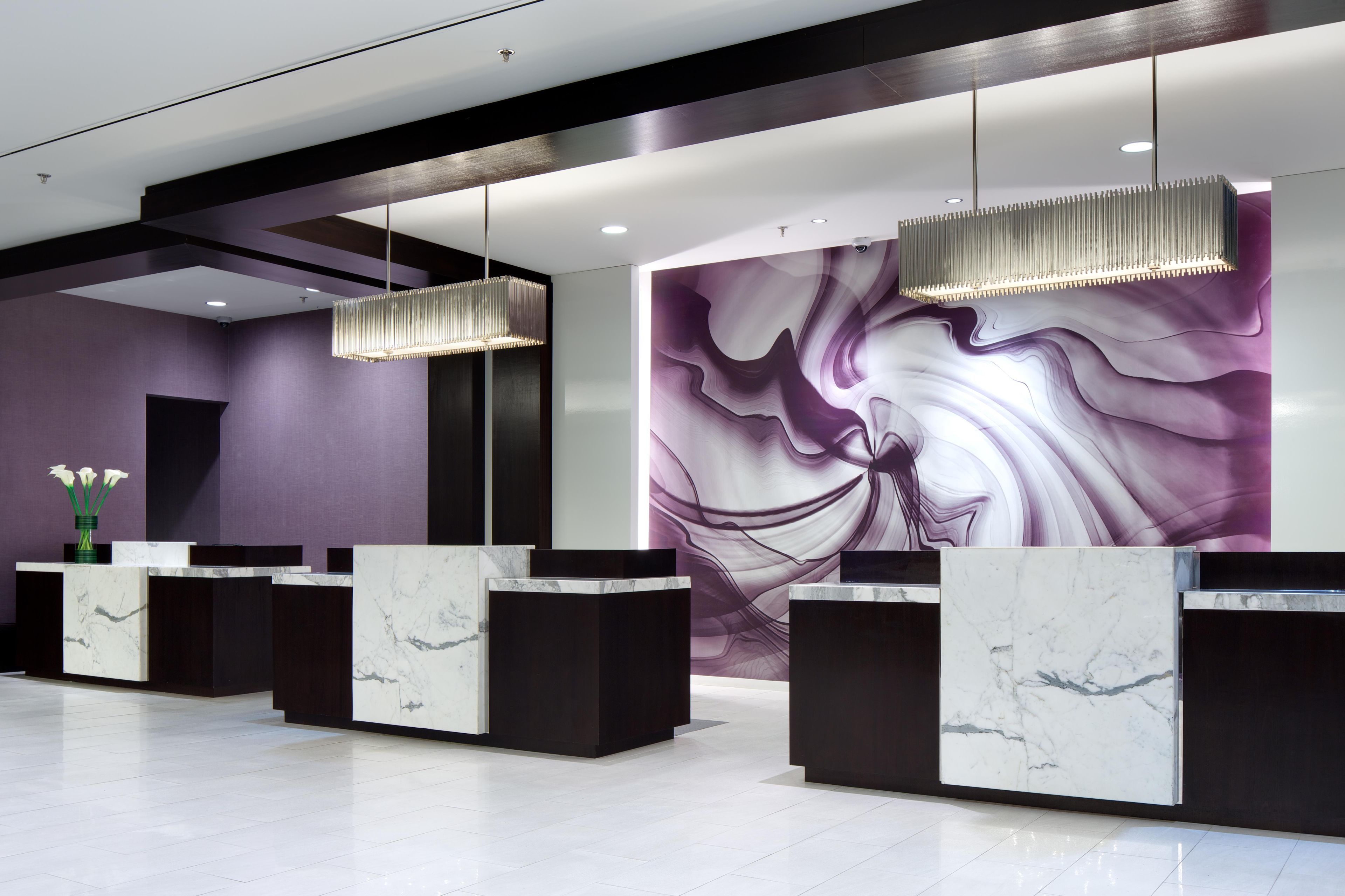 Un área de recepción con mostradores de mármol, iluminación colgante y un amplio mural abstracto en la pared.