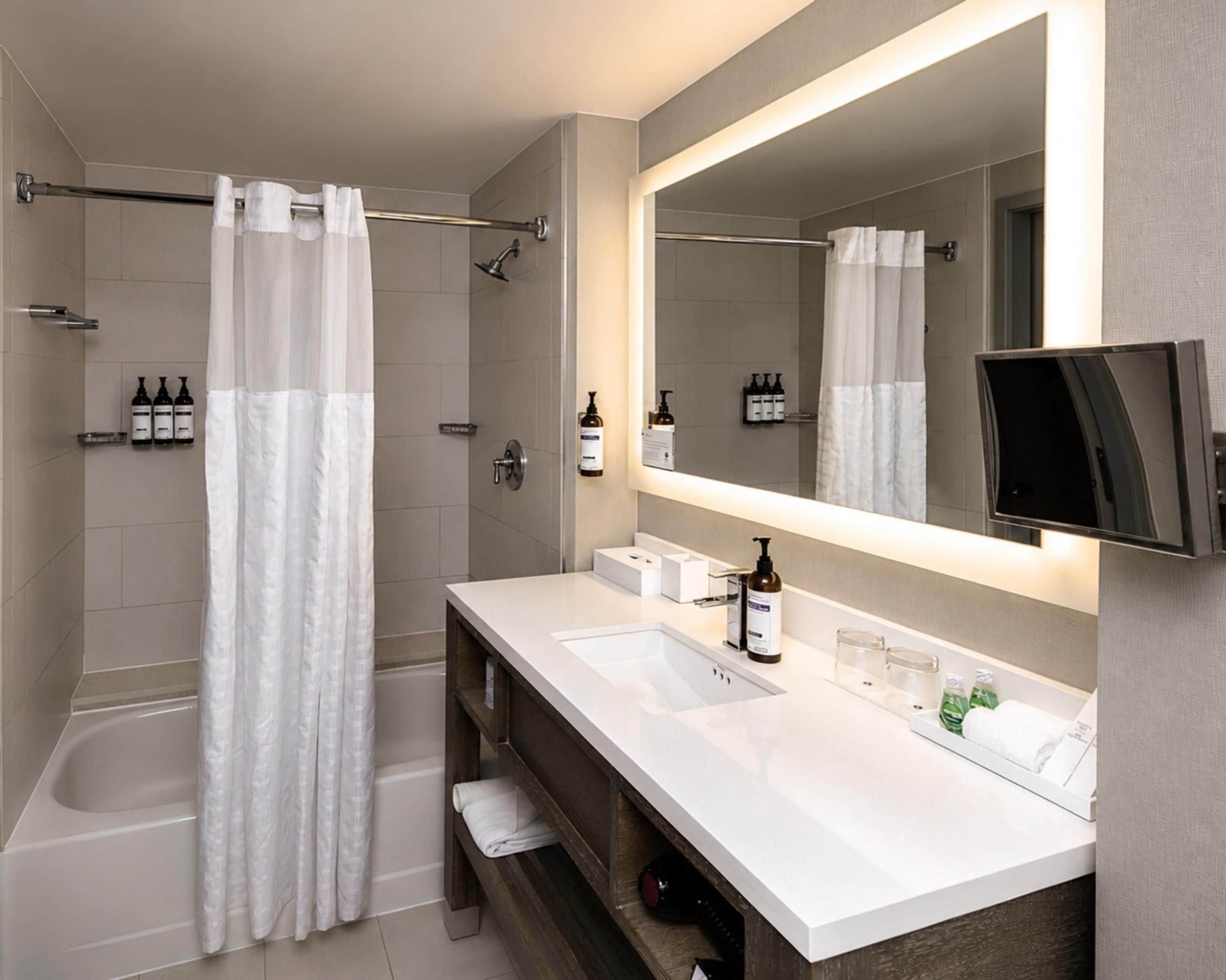 A modern bathroom with a shower, a large mirror, and a vanity with a sink.