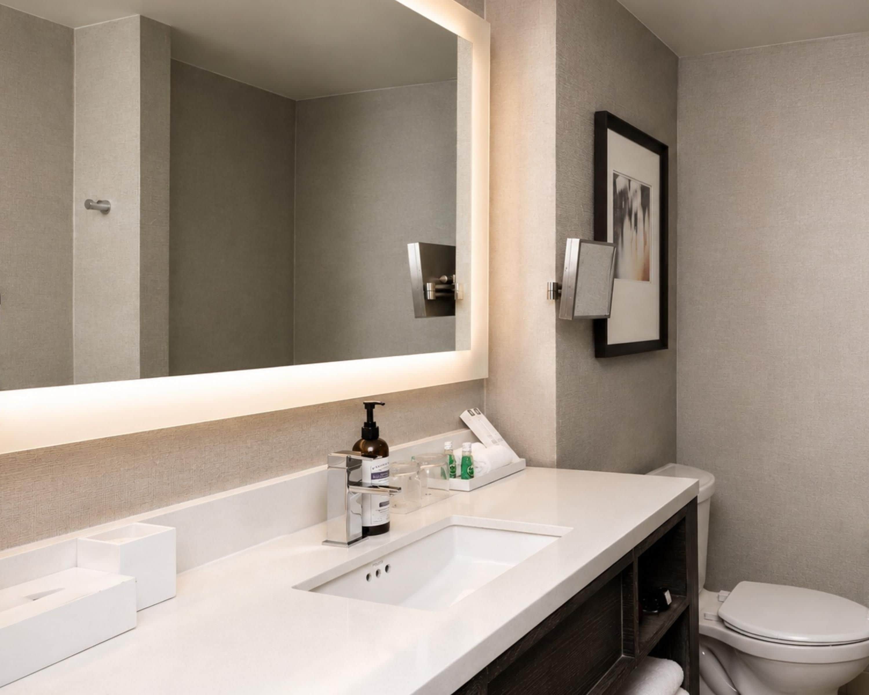 A modern bathroom with a large mirror, a white sink, and a toilet.