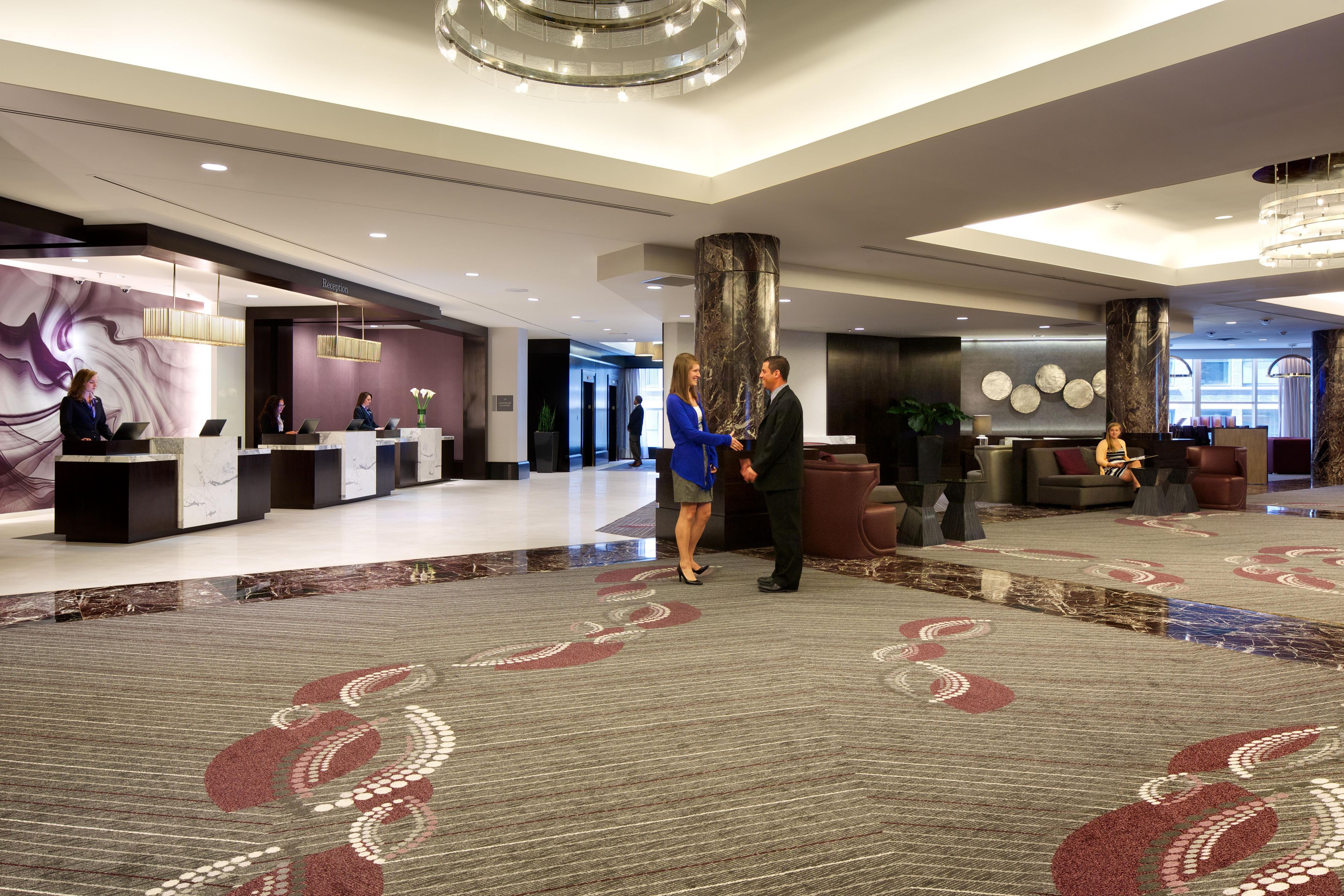 A hotel lobby with a reception desk, a large marble column, and a patterned carpet.