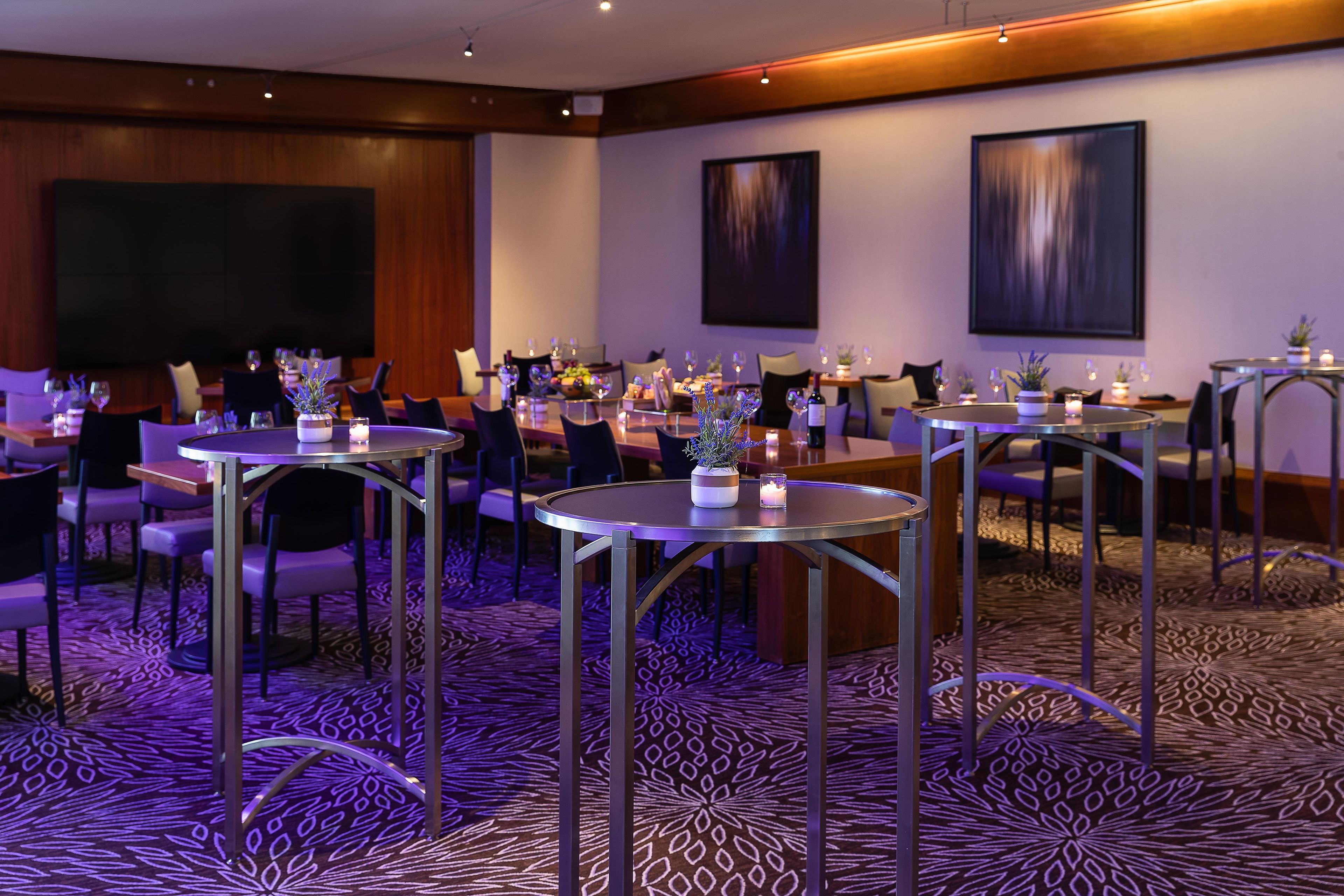 A hotel dining area with round tables, chairs, and a carpeted floor.