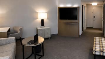 A hotel room with a flat-screen TV mounted on a wall, a small table with a laptop, a chair, a sofa, and a bed.