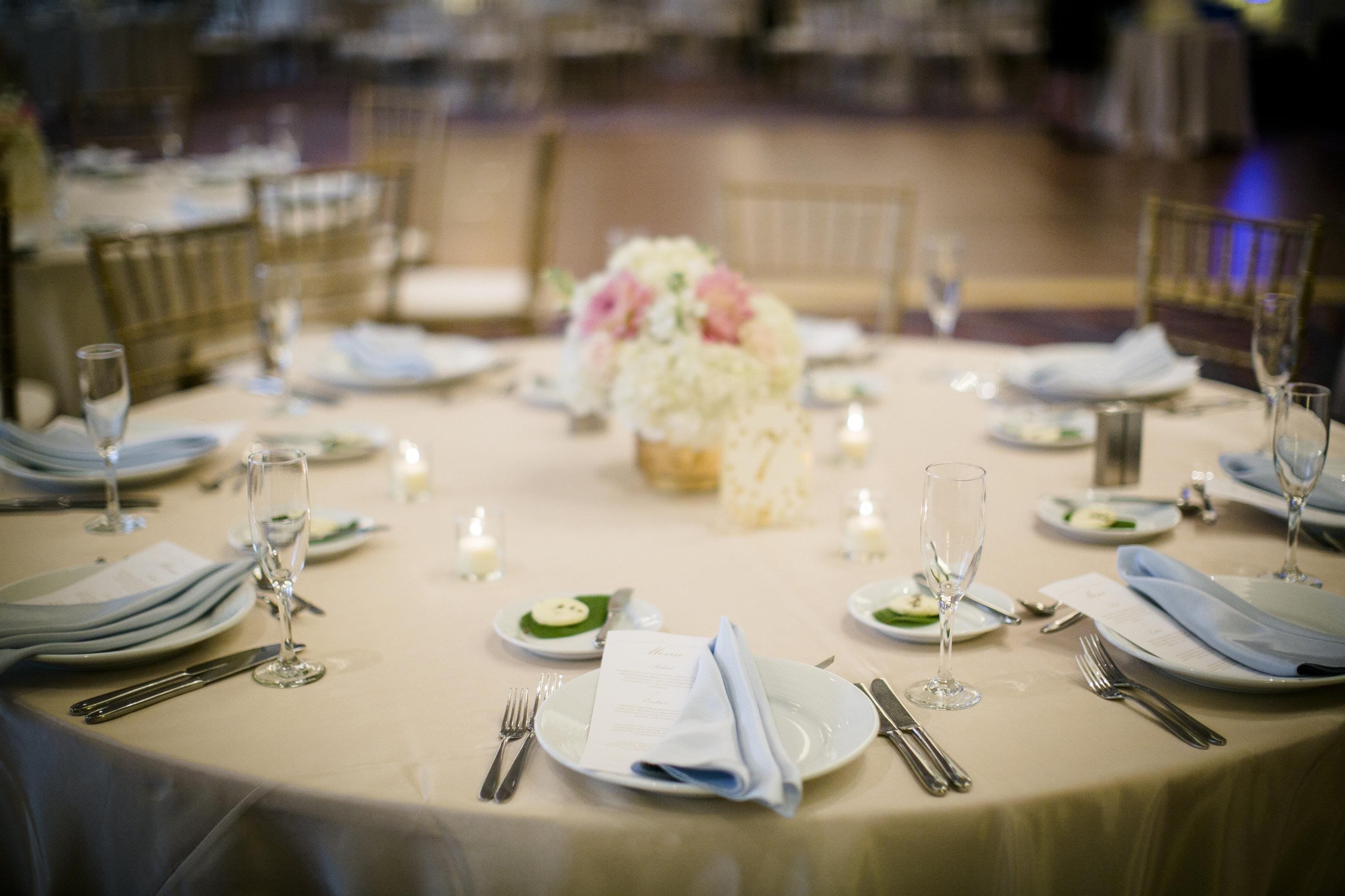 A round dining table set for a formal event with multiple place settings, glasses, and a centerpiece.