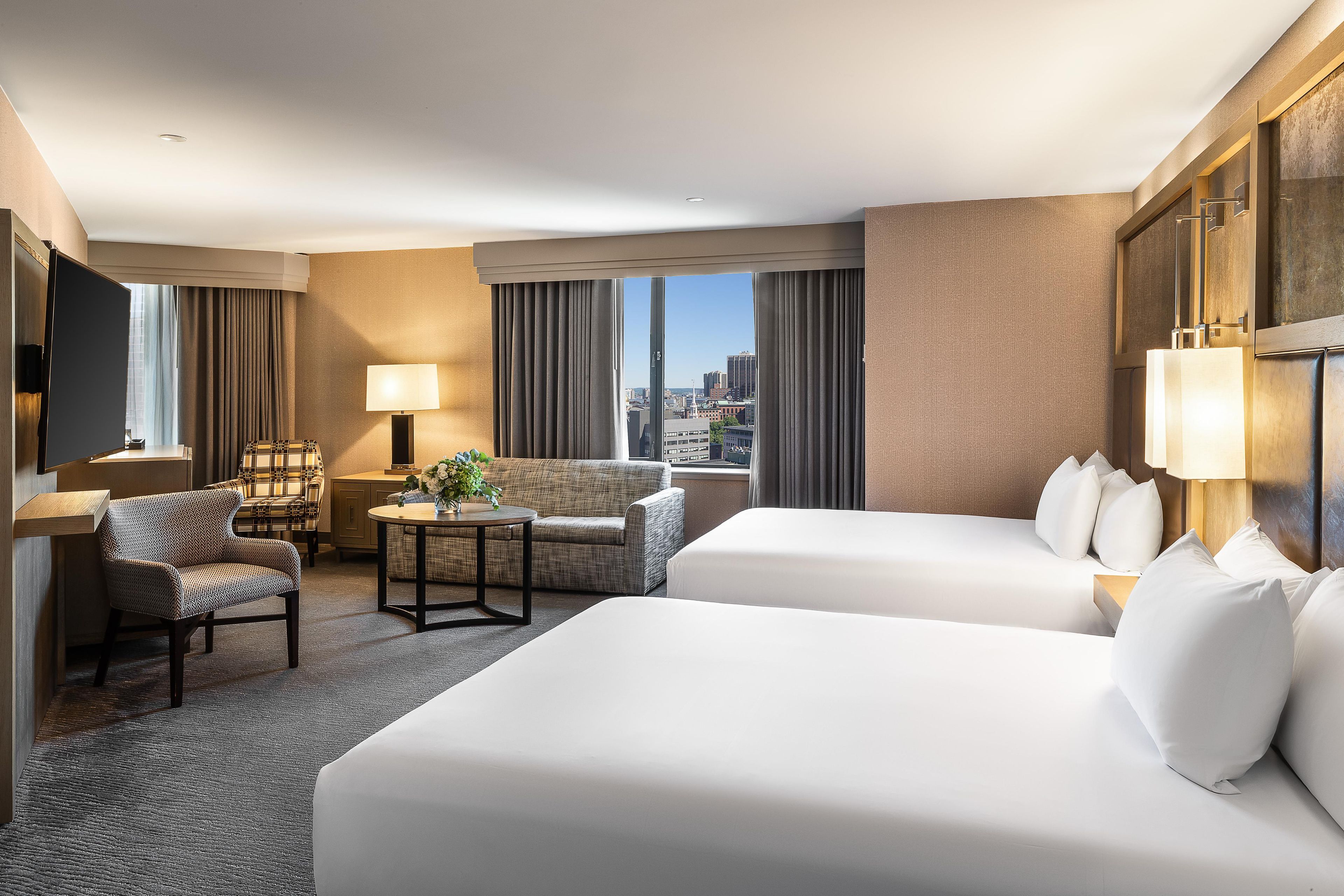 A hotel room with two beds, a sofa, a chair, a small table, and a TV.
