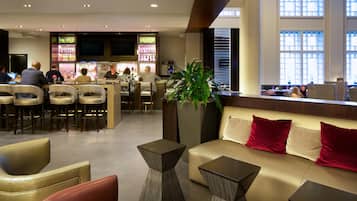 A hotel lobby with a bar area, seating arrangements, and a large window providing natural light.