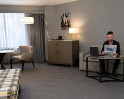 A hotel room with a sofa, a chair, a table, a lamp, a cabinet, and a bed.