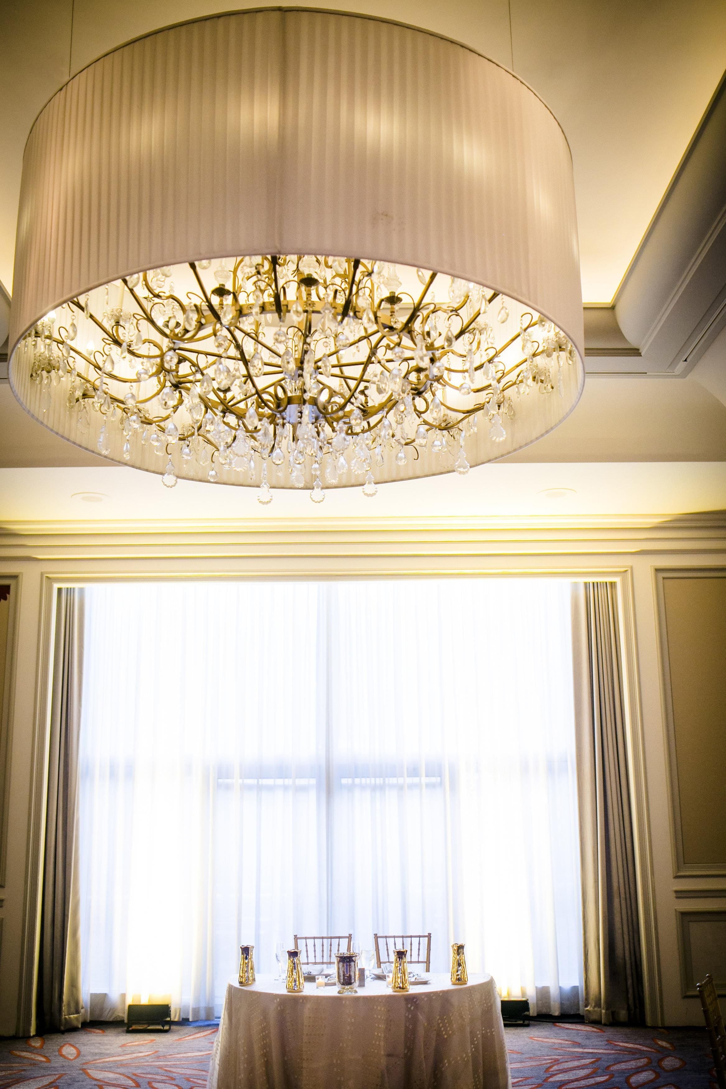 A room with a large chandelier, a table set for dining, and a view through a large window.