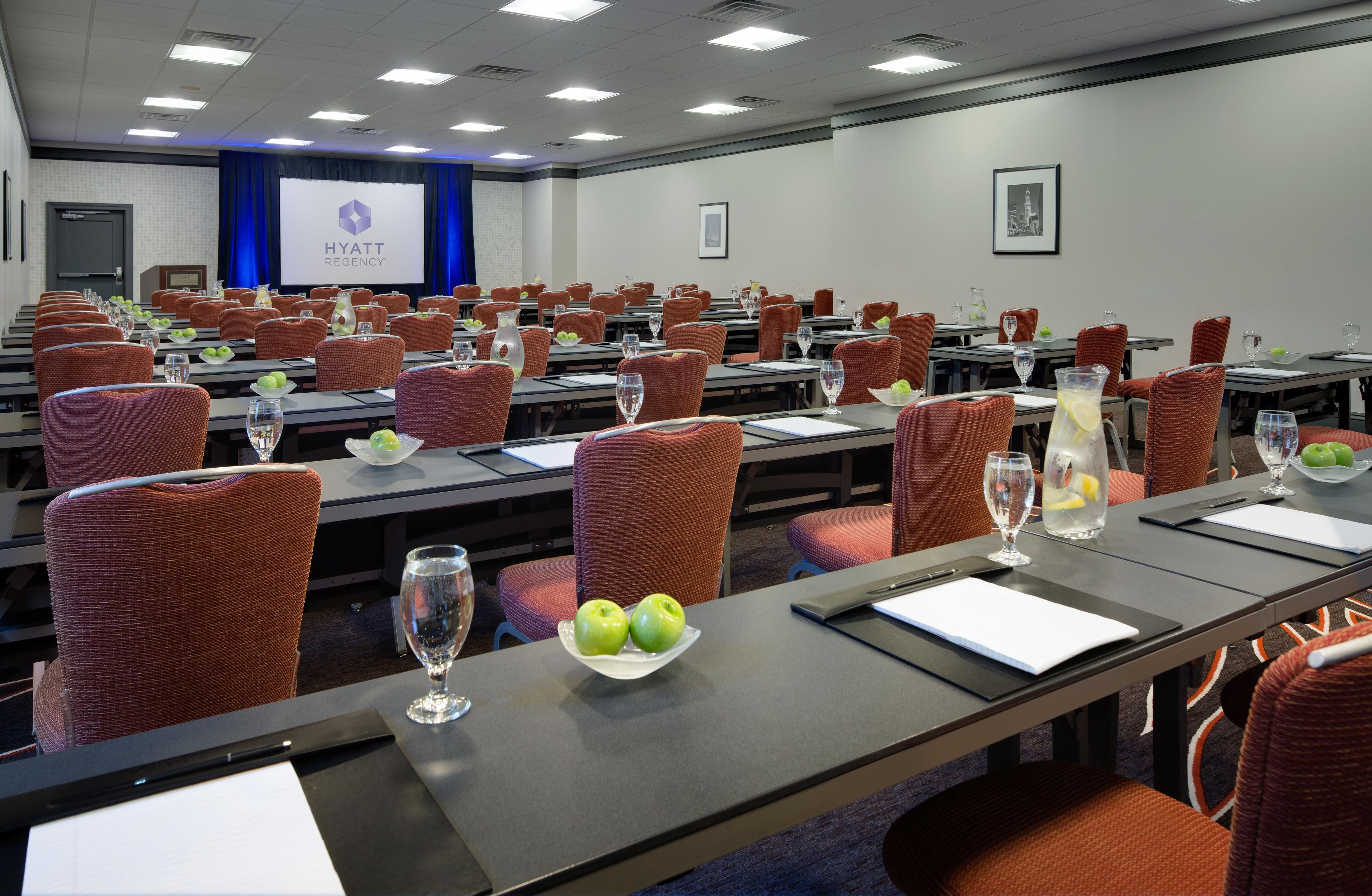 A conference room with rows of tables, chairs, and presentation screens.