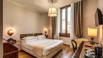 Quarto de hotel com uma cama grande, abajures, uma mesa de trabalho com cafeteira e vista para o exterior pela janela.