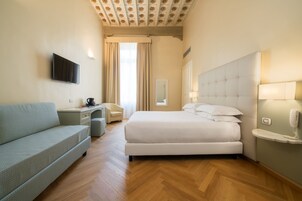 Una habitación de hotel con cama, sofá, escritorio, televisor y espejo.