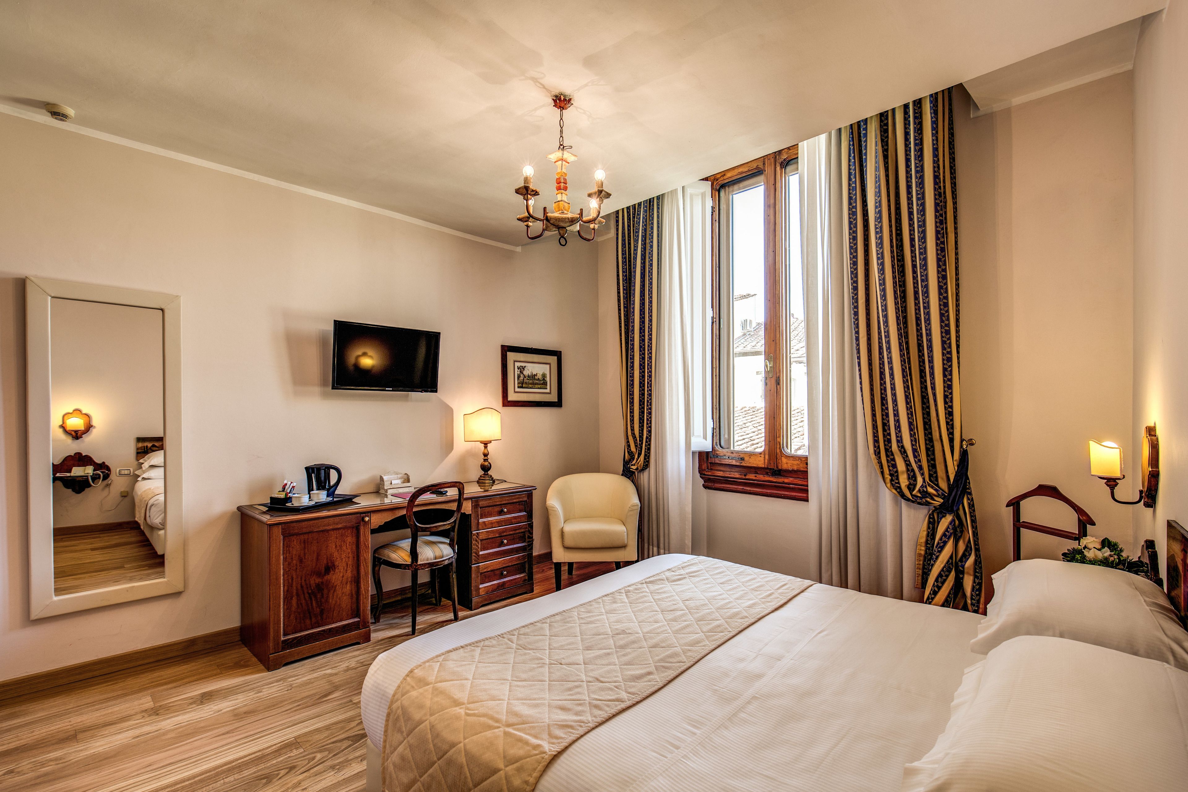 Quarto de hotel com uma cama grande, uma escrivaninha com cadeira, uma televisão e um espelho.