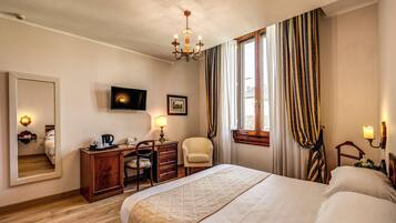 Quarto de hotel com uma cama grande, uma escrivaninha com cadeira, uma televisão e um espelho.