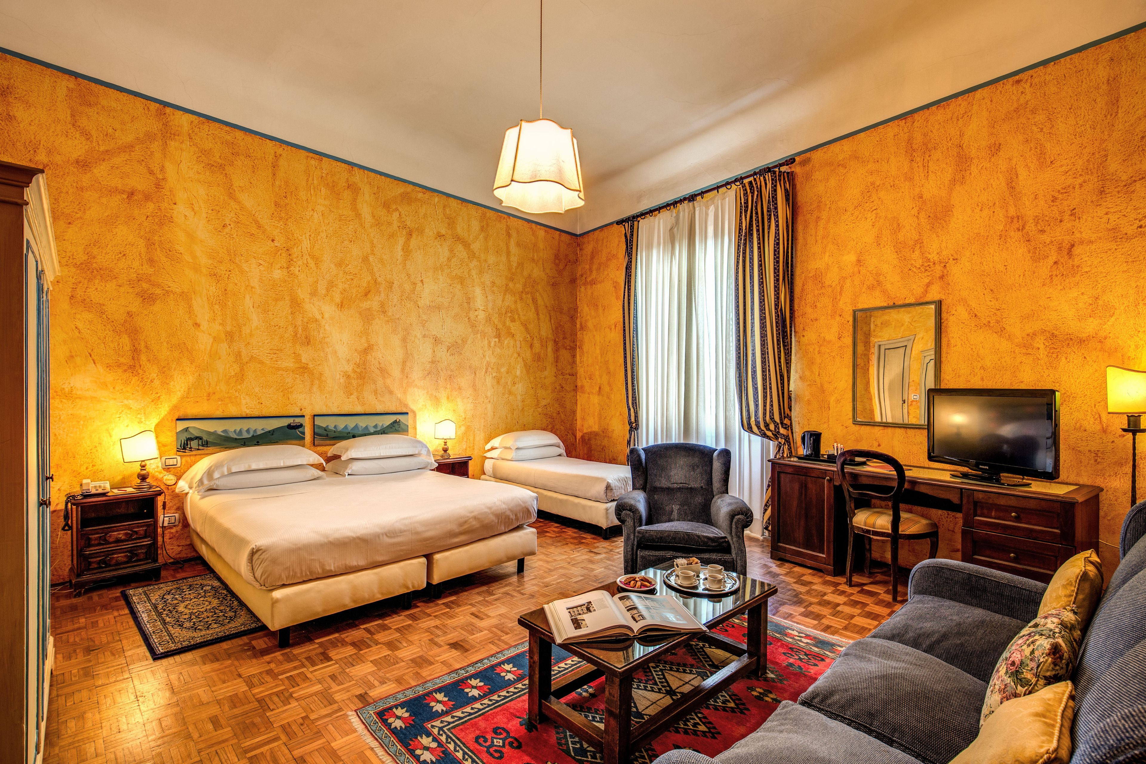 A hotel room with two beds, a sofa, a television, and a desk.