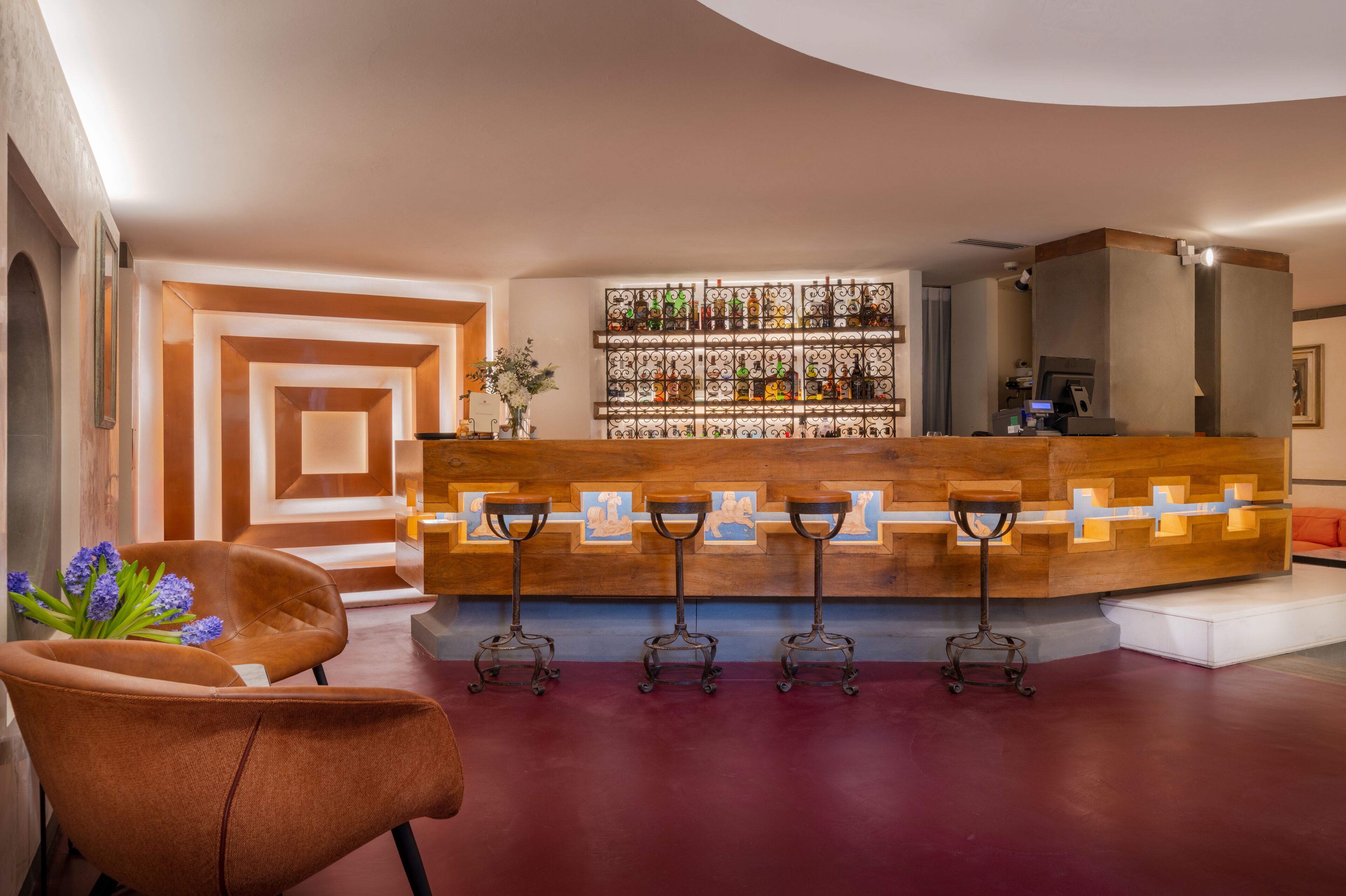 Una zona de bar con un mostrador de madera, tres taburetes y una pared llena de botellas de licor.