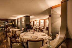 Un restaurante con mesas redondas, sillas de madera y una zona de bar.