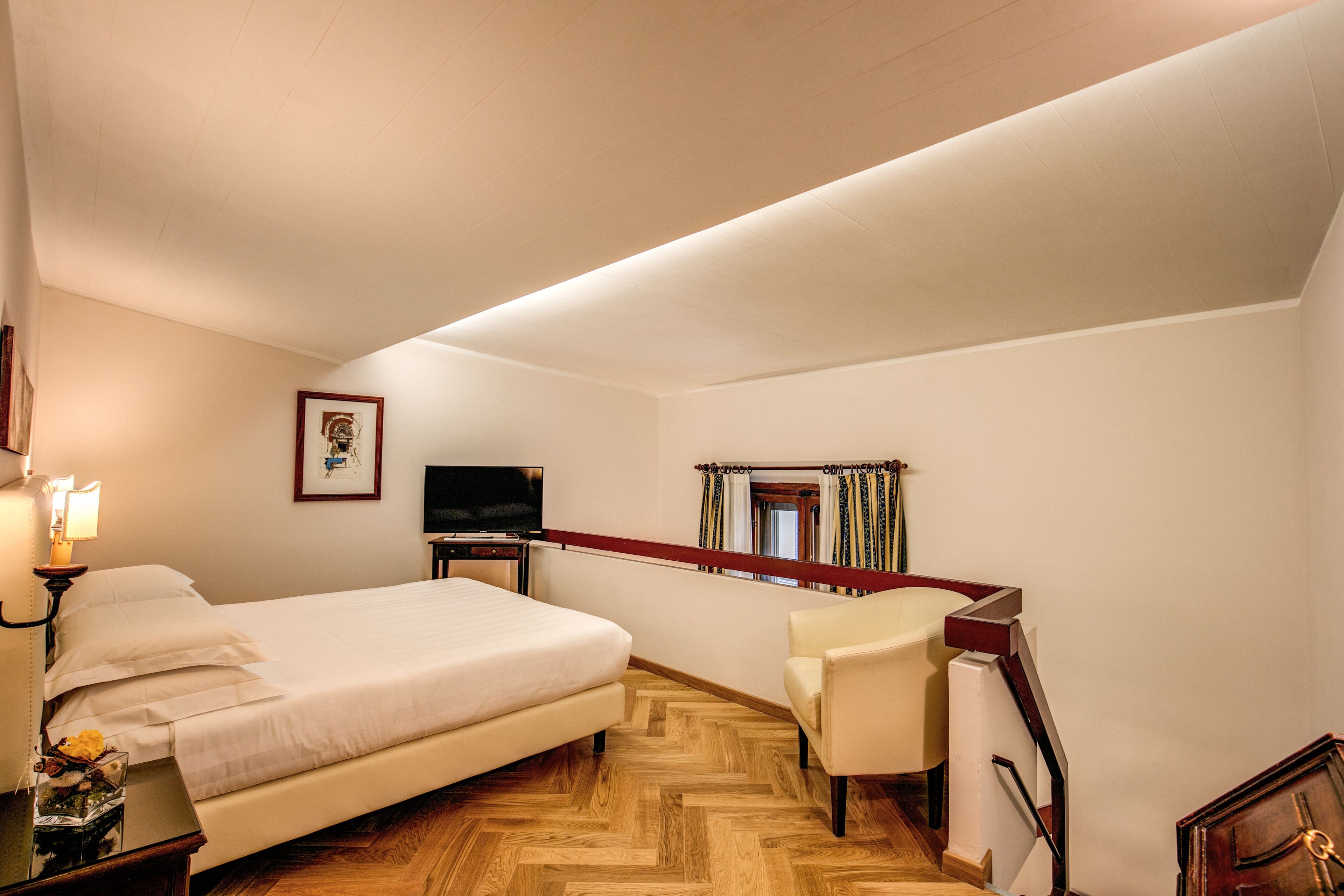 A hotel room with a bed, a desk, a chair, a TV, and a window with curtains.