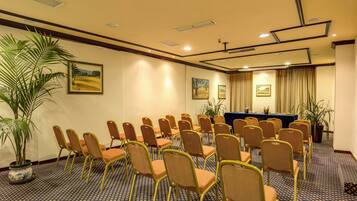 A conference room with rows of chairs, a table, and potted plants.