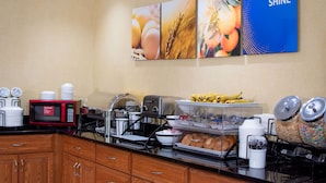 A breakfast bar with a microwave, toaster, and various food items. There are also several food containers and a coffee machine.