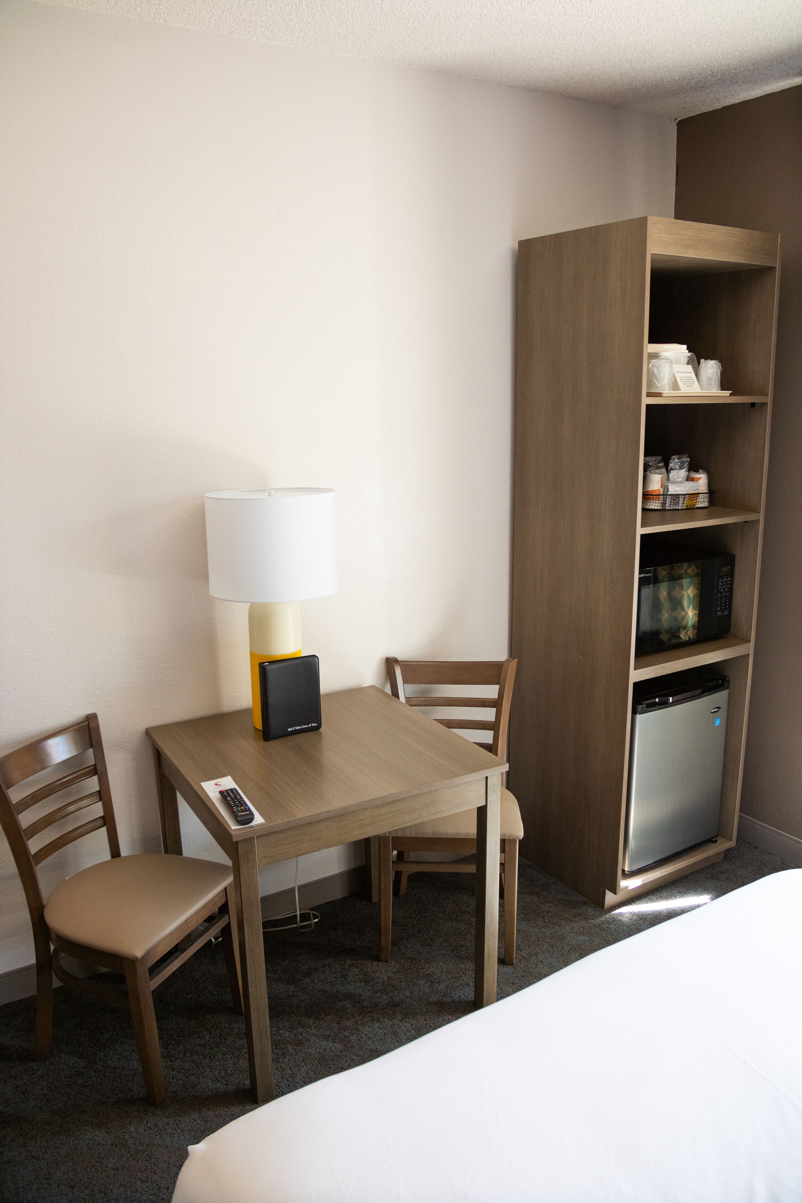 Une chambre d’hôtel avec un bureau en bois, deux chaises, une lampe, un mini-bar et un lit.