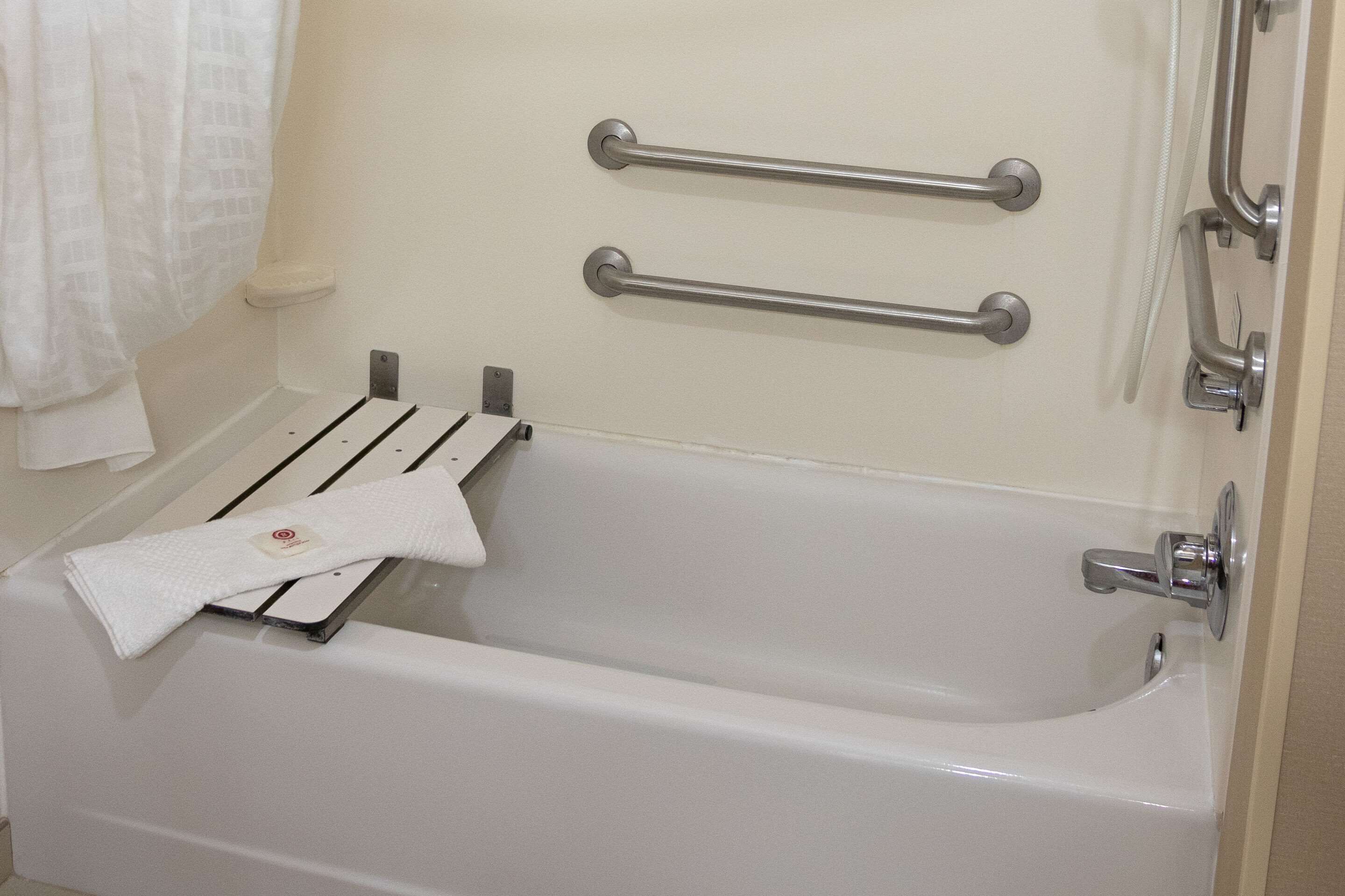 A white bathtub with two metal grab bars, a towel rack, and a shower control panel.