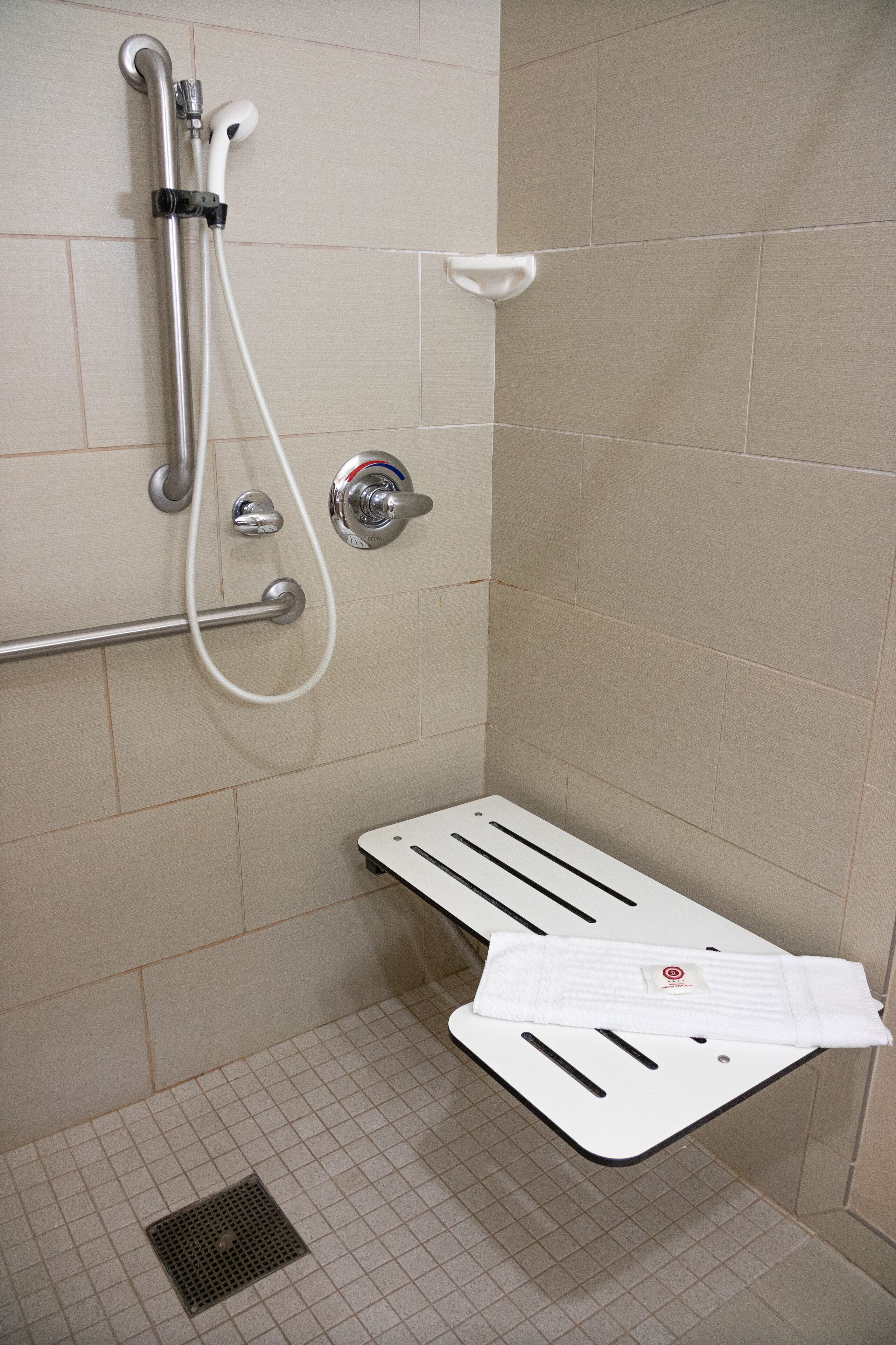 A shower area with a grab bar, a handheld showerhead, and a white towel on a shelf.