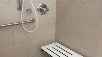 A shower area with a grab bar, a handheld showerhead, and a white towel on a shelf.