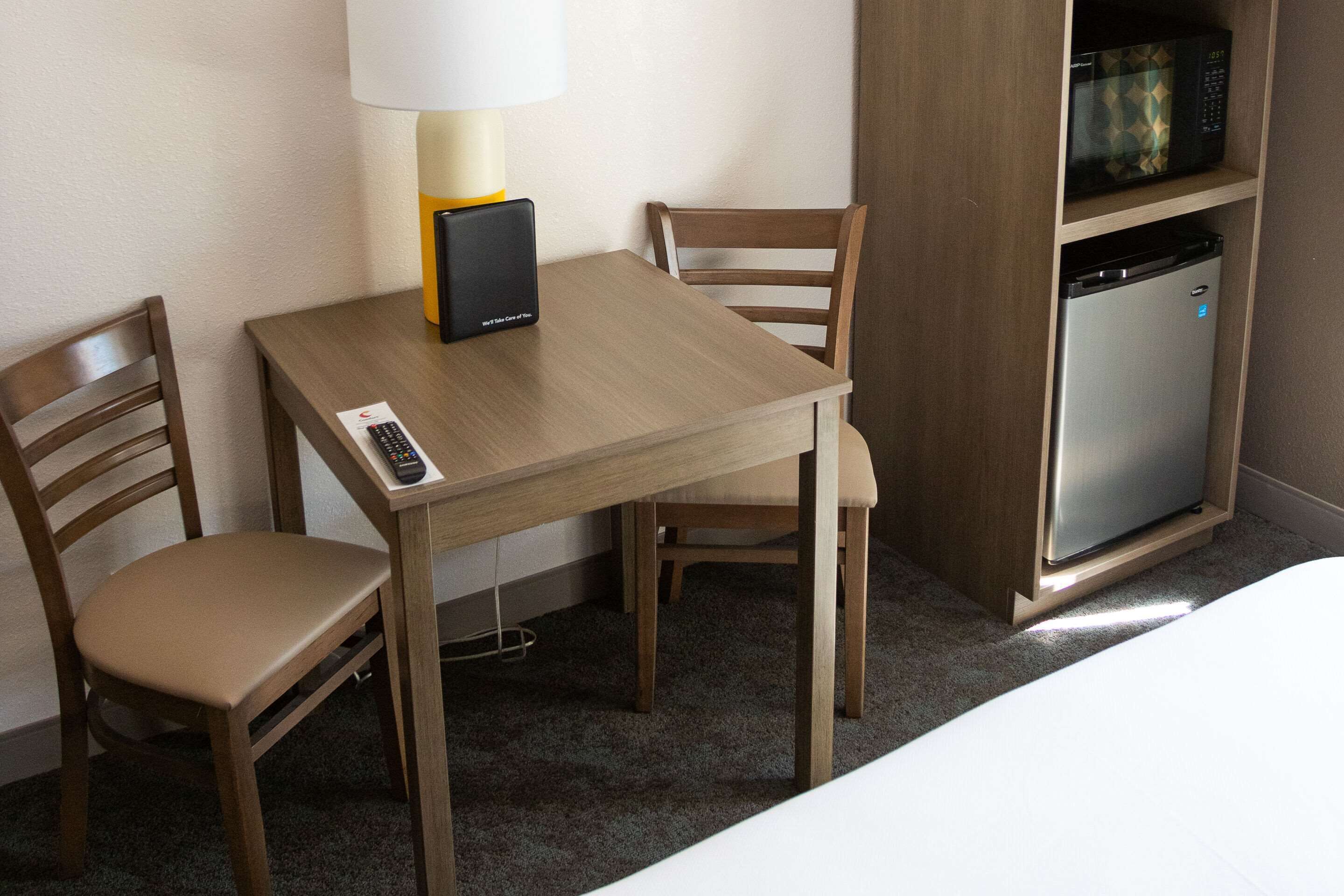 Une chambre d’hôtel avec une table en bois, deux chaises, une lampe, un four à micro-ondes et un mini-réfrigérateur.