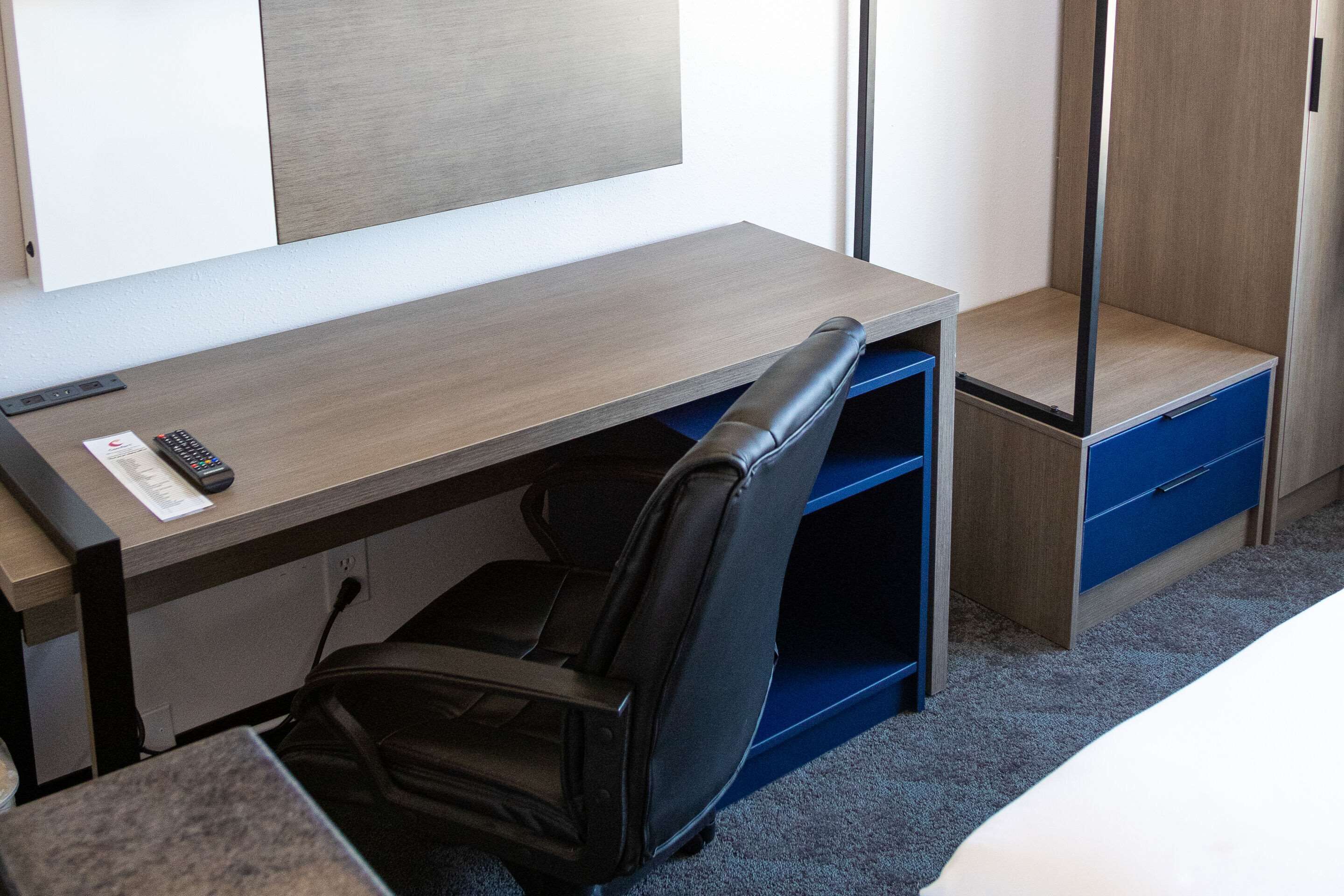 A hotel room with a desk, a chair, a wardrobe, and a bed.