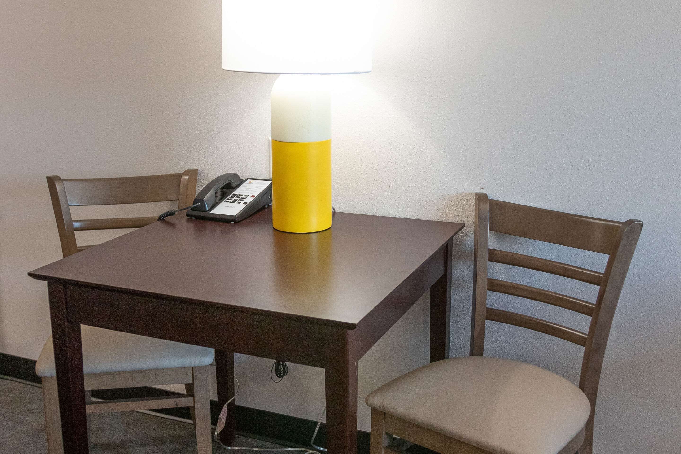 A wooden table with a lamp, a telephone, and two chairs.